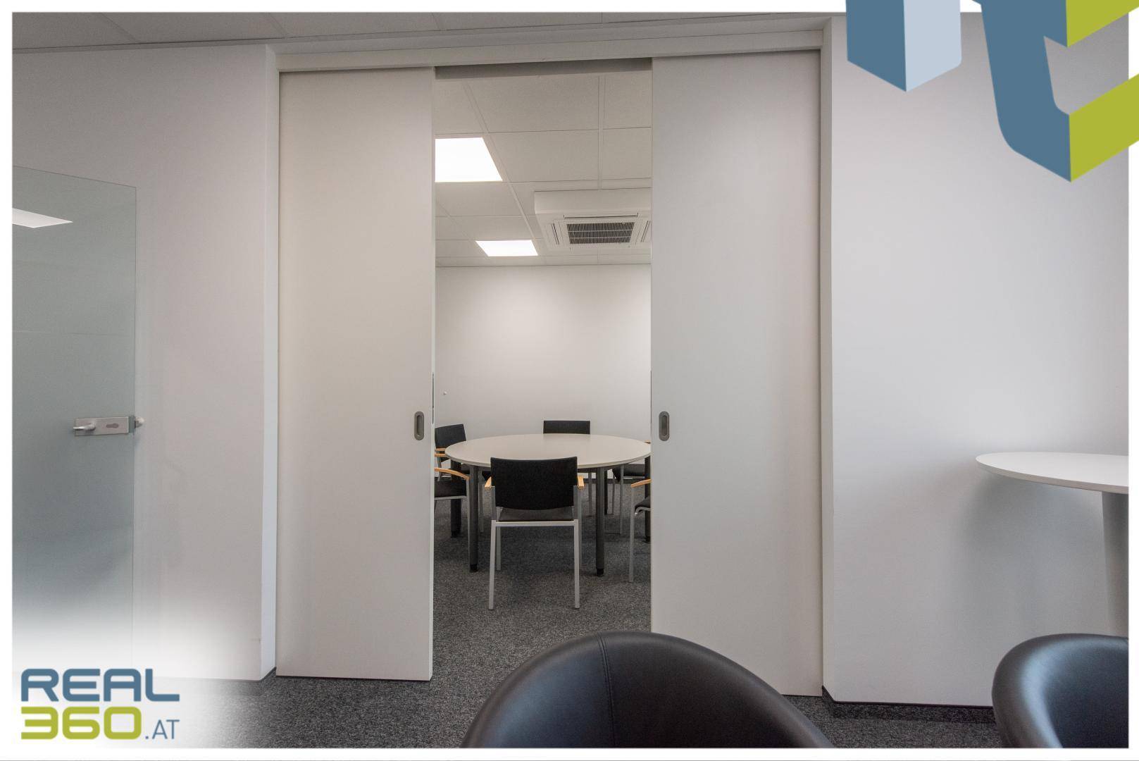 Besprechungsraum mit Schiebetüren, einem runden Tisch und Stühlen, bereit für Meetings.