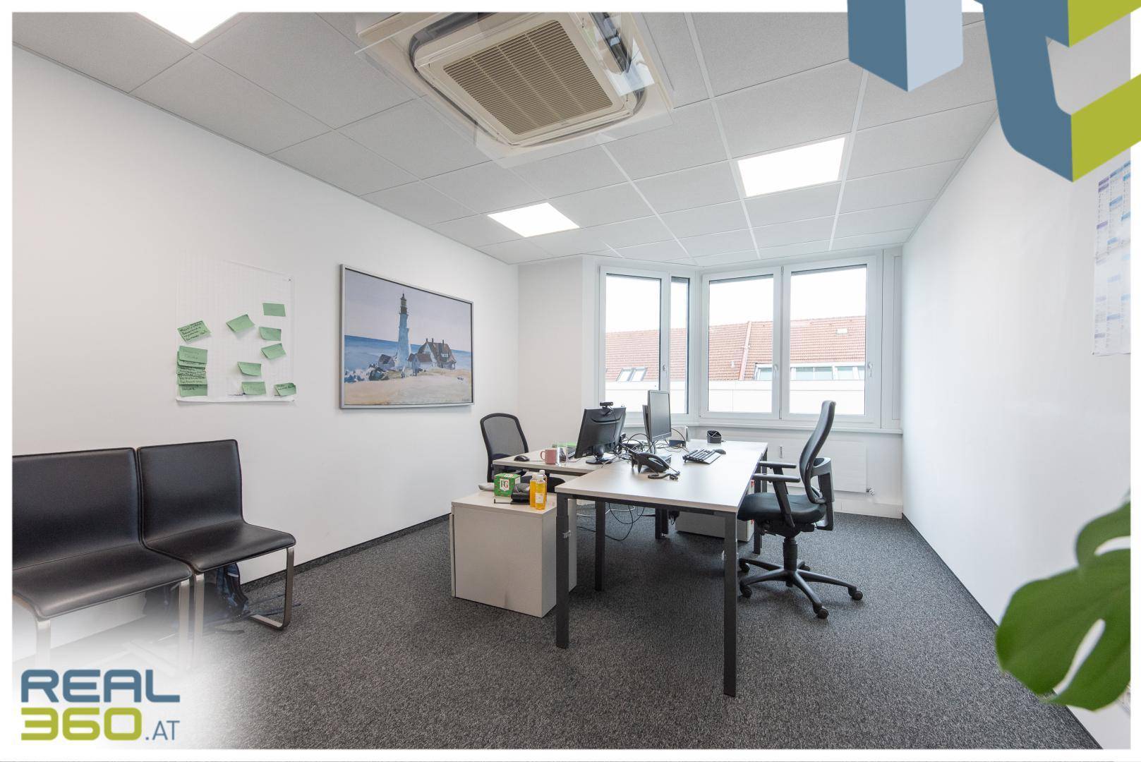 Helles Büro mit Schreibtisch, Bürostühlen und großen Fenstern, die viel Tageslicht hereinlassen.