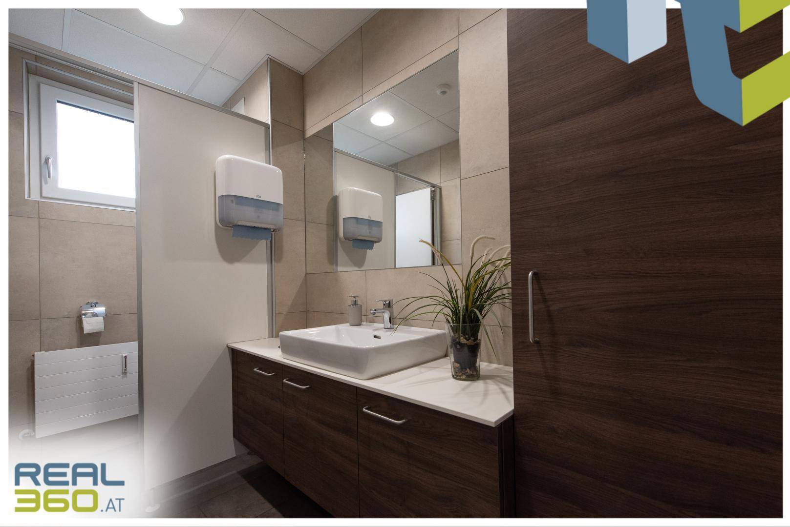 Modernes Badezimmer mit Waschbecken, Spiegel und beigen Fliesen an den Wänden.