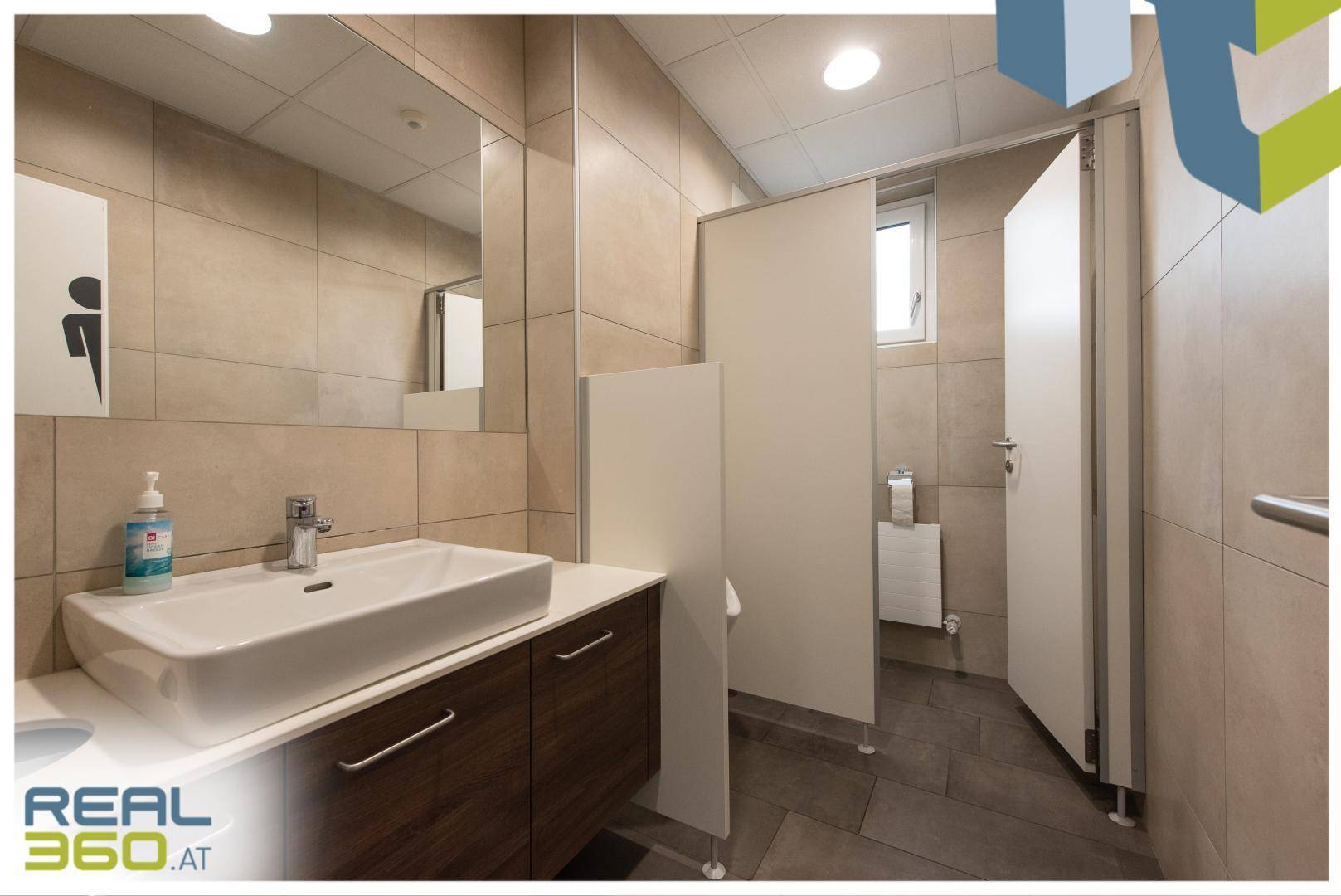Modernes Badezimmer mit Waschbecken, Spiegel und beigen Fliesen an den Wänden.