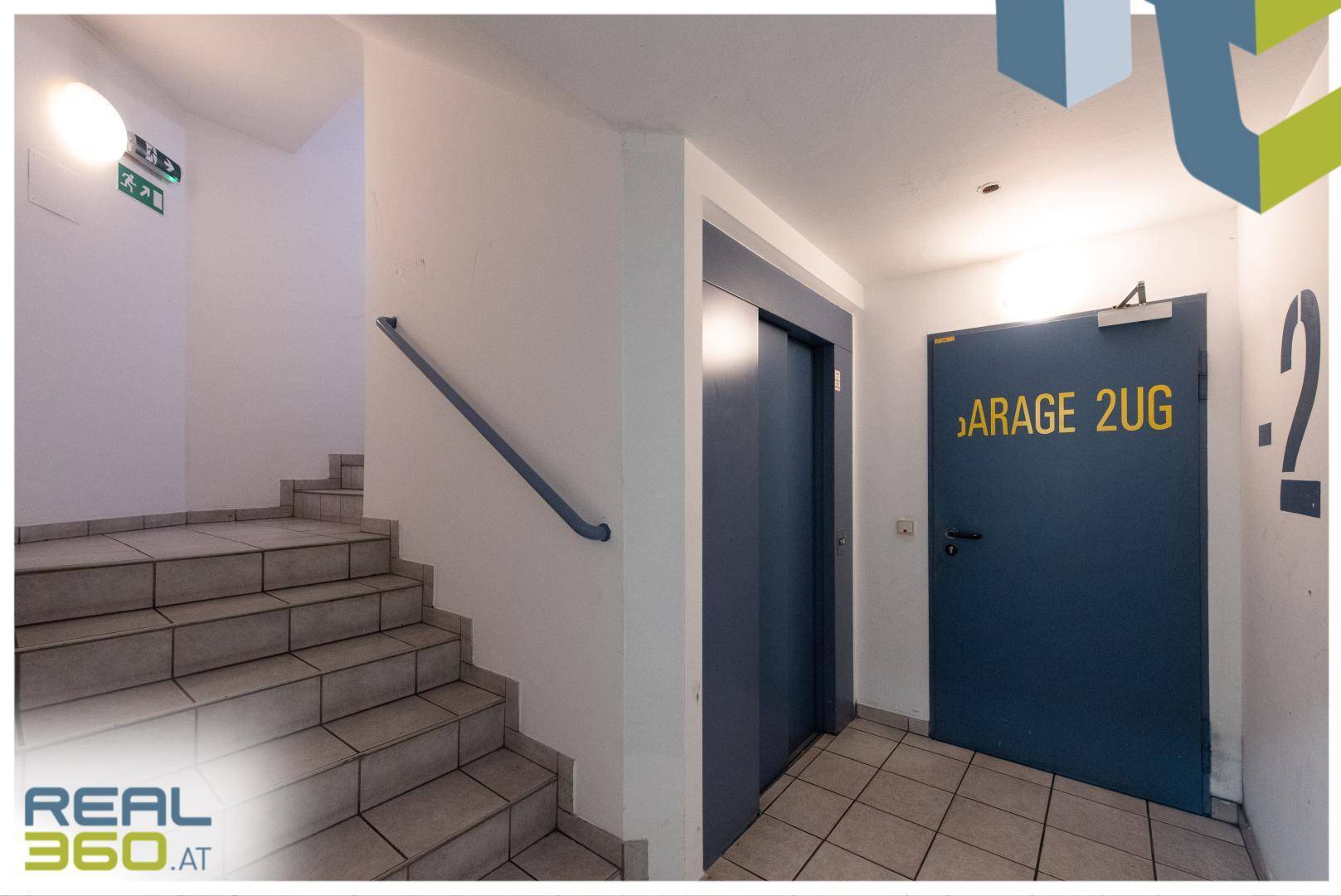 Treppenhaus mit Steinstufen, Handlauf und einem Aufzug, der die Etagen verbindet.
