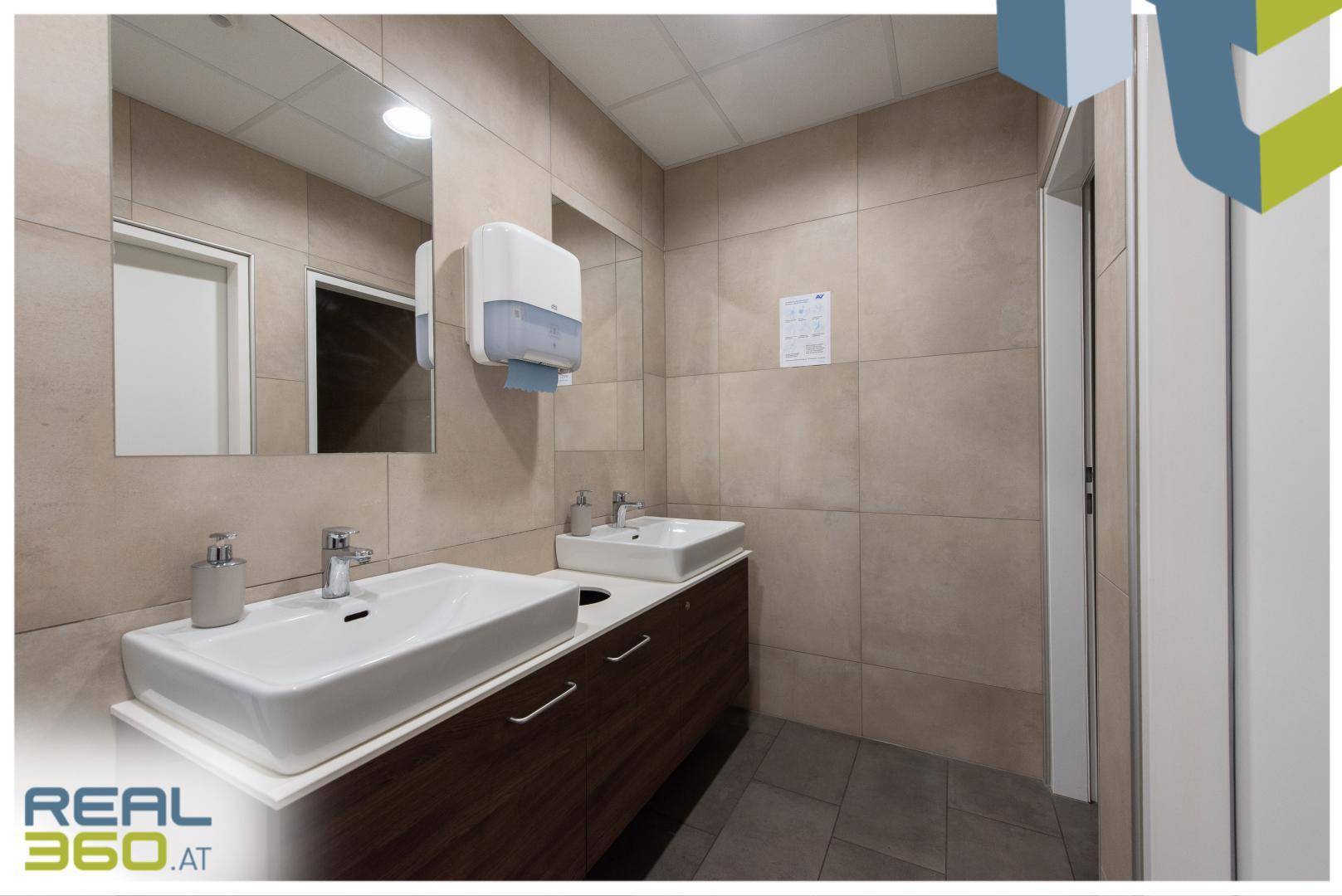 Modernes Badezimmer mit zwei Waschbecken, Holzunterschränken und beigen Fliesen an den Wänden.