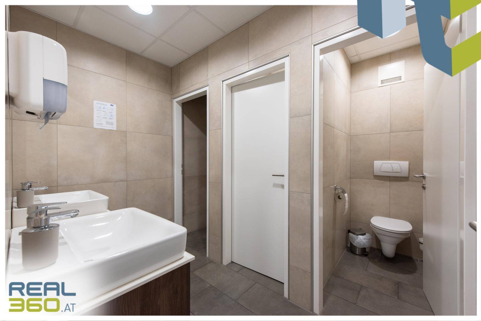 Helles Badezimmer mit zwei Waschbecken, großen Spiegeln und beigen Fliesen an den Wänden.