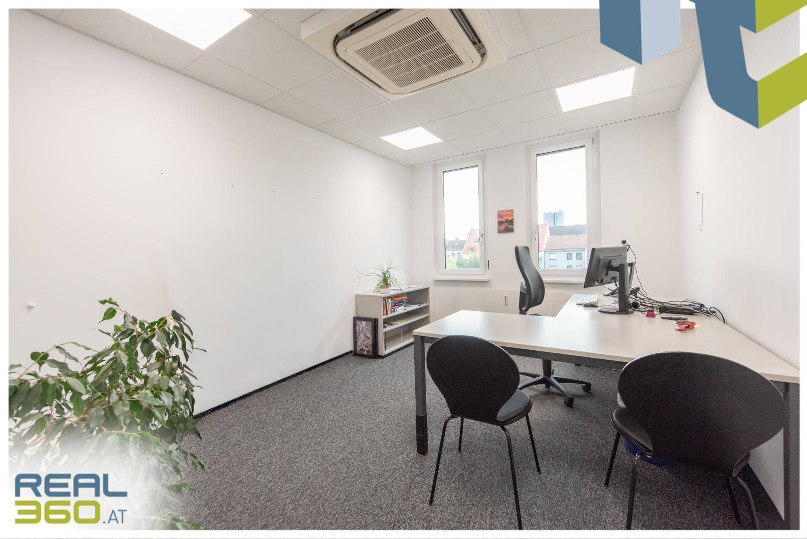 Helles Büro mit Schreibtisch, Bürostuhl, Regal und Fenstern, die viel Tageslicht hereinlassen.