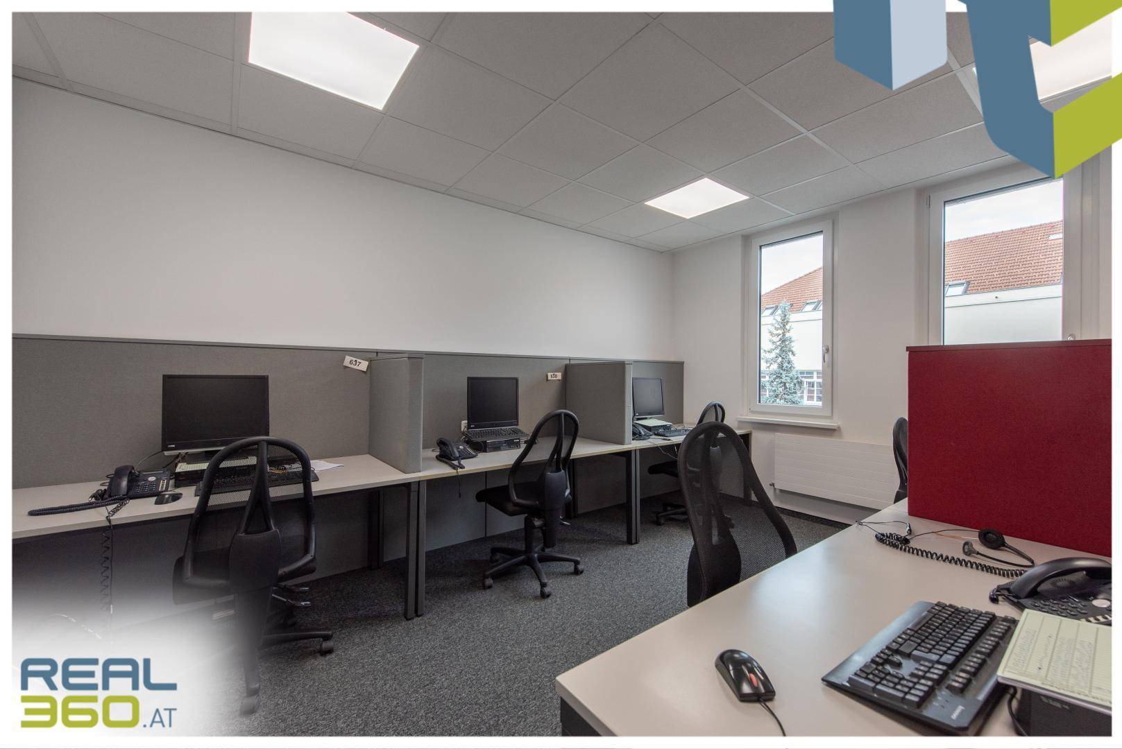 Reihe von Arbeitsplätzen mit Trennwänden, Computern und Fenstern, die Tageslicht spenden.