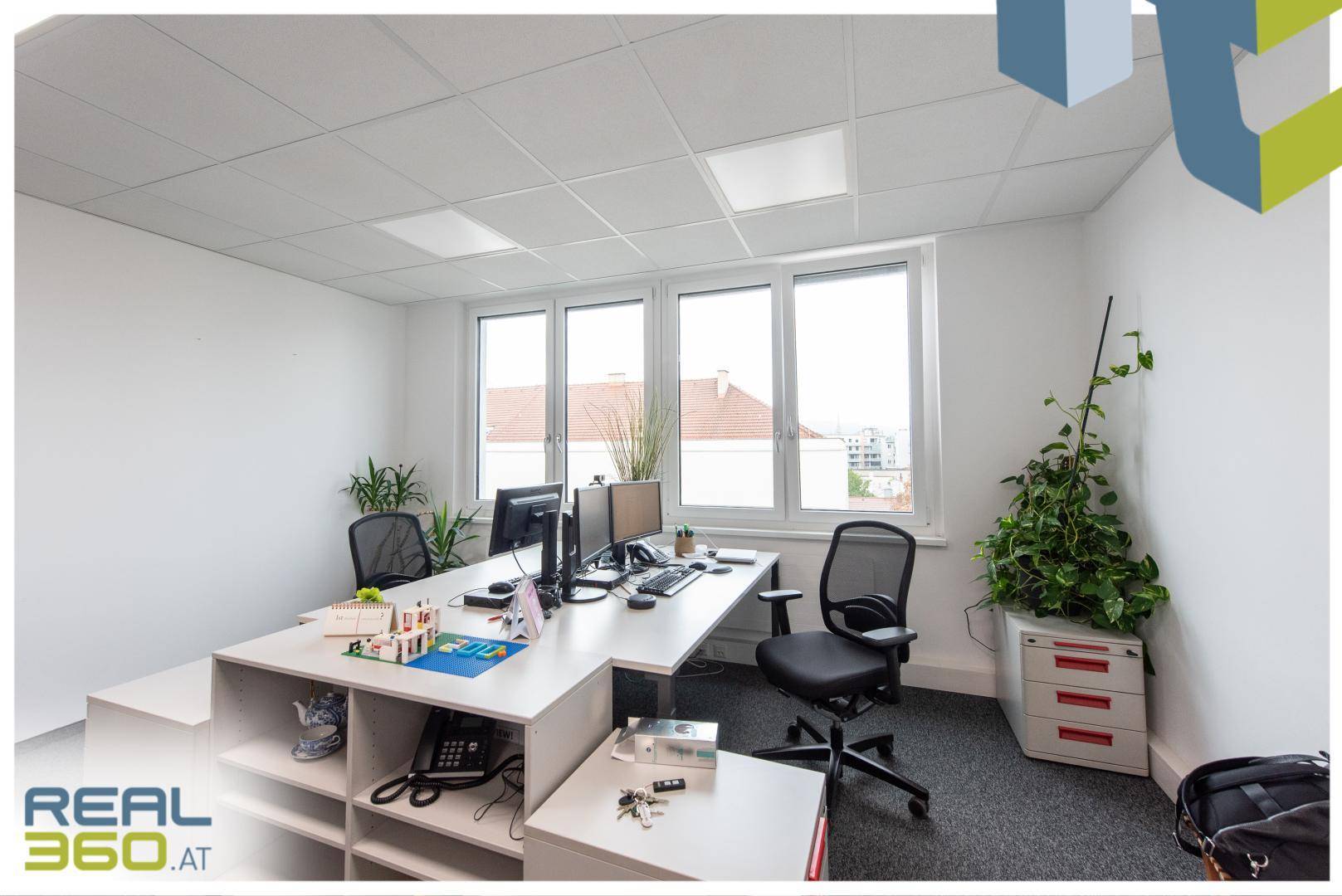 Büro mit Eckschreibtisch, Bürostuhl und großen Fenstern, die viel Tageslicht hereinlassen und eine weite Aussicht bieten.