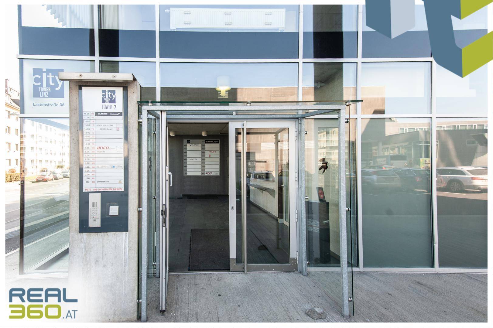 Moderner Eingangsbereich eines Bürogebäudes mit großen Glasfronten und Beschilderung.