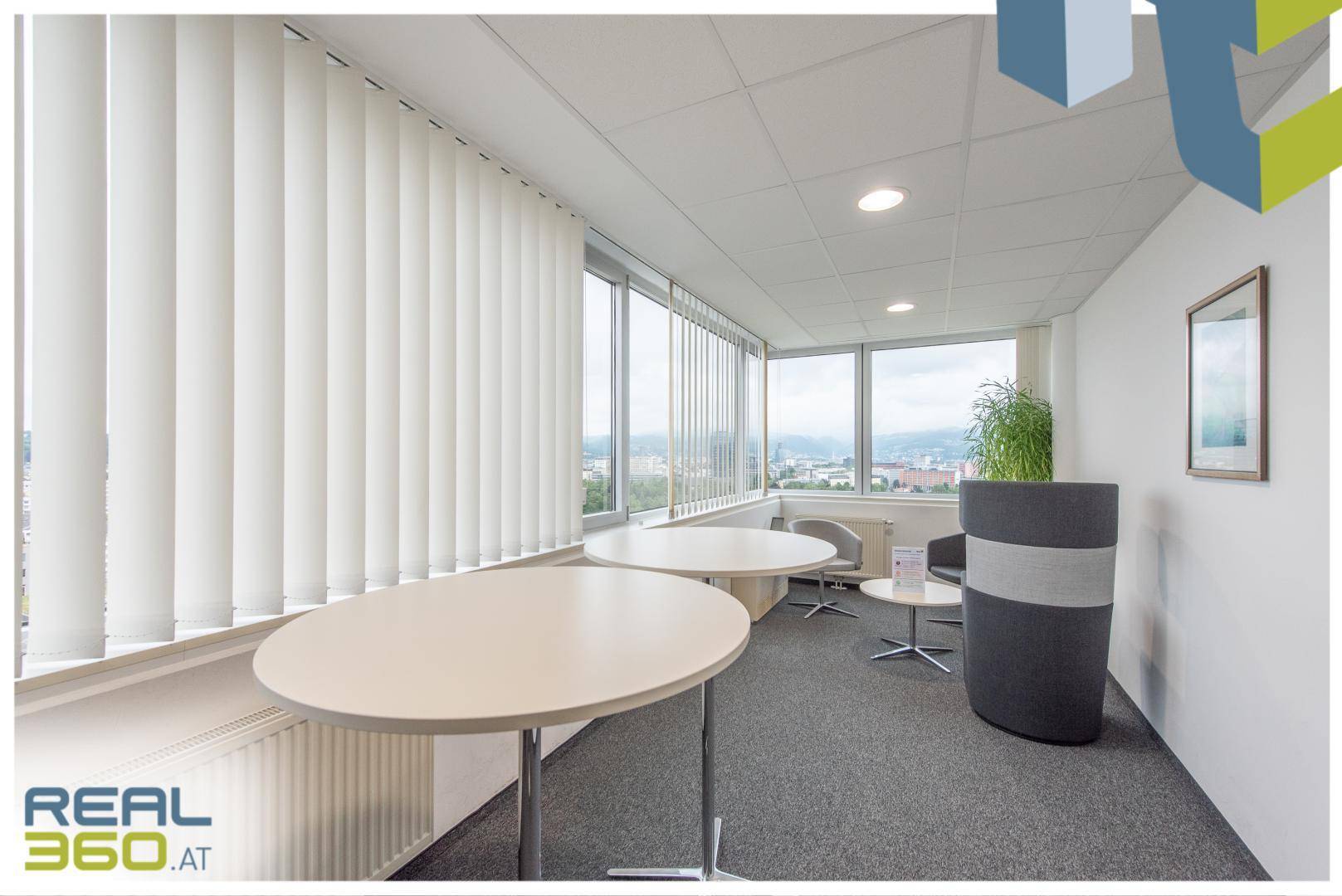 Heller Loungebereich im Büro mit runden Tischen, bequemen Sitzelementen und großen Fenstern.