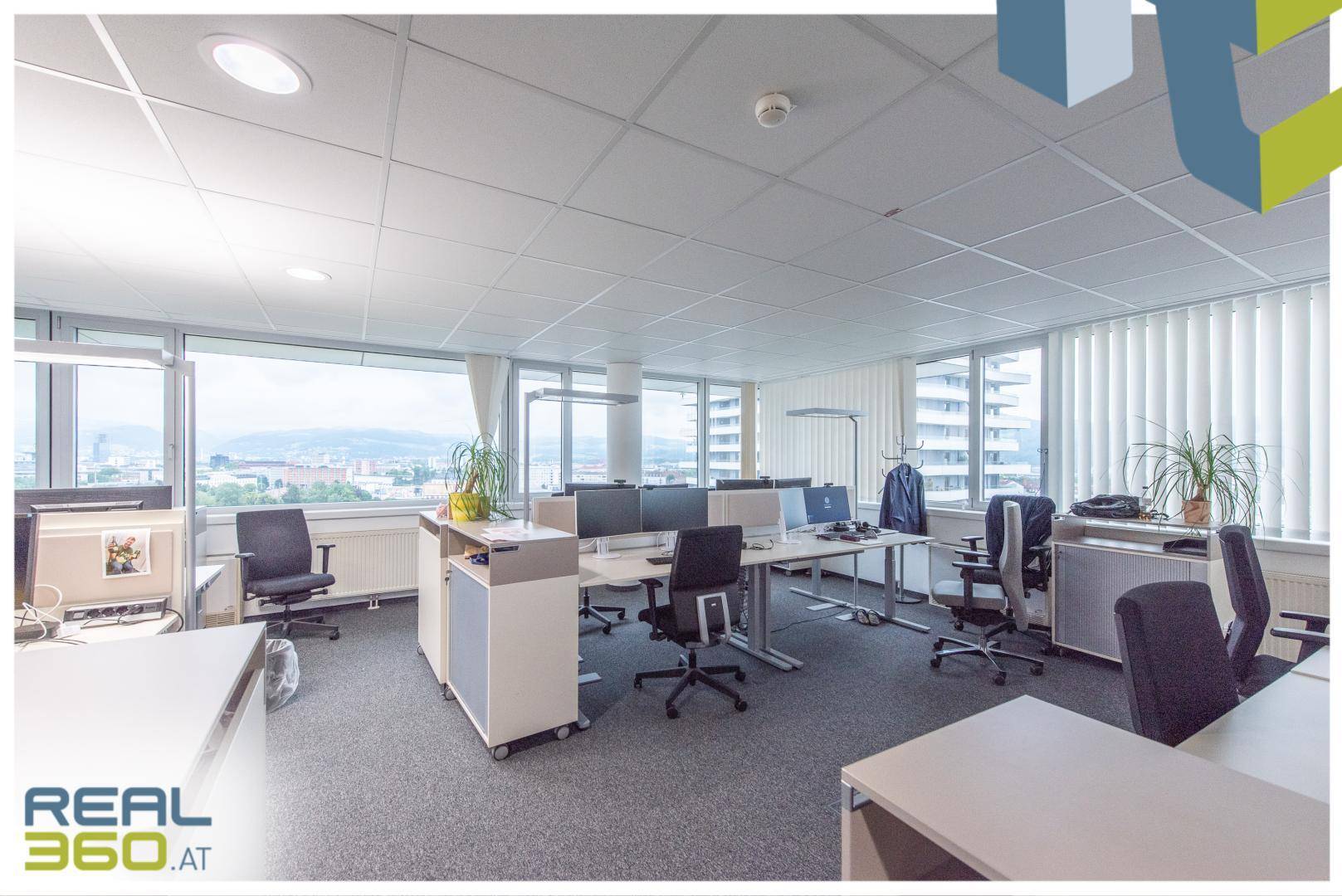Großraumbüro mit mehreren Arbeitsplätzen, großen Fenstern und Panoramablick auf die Stadt.