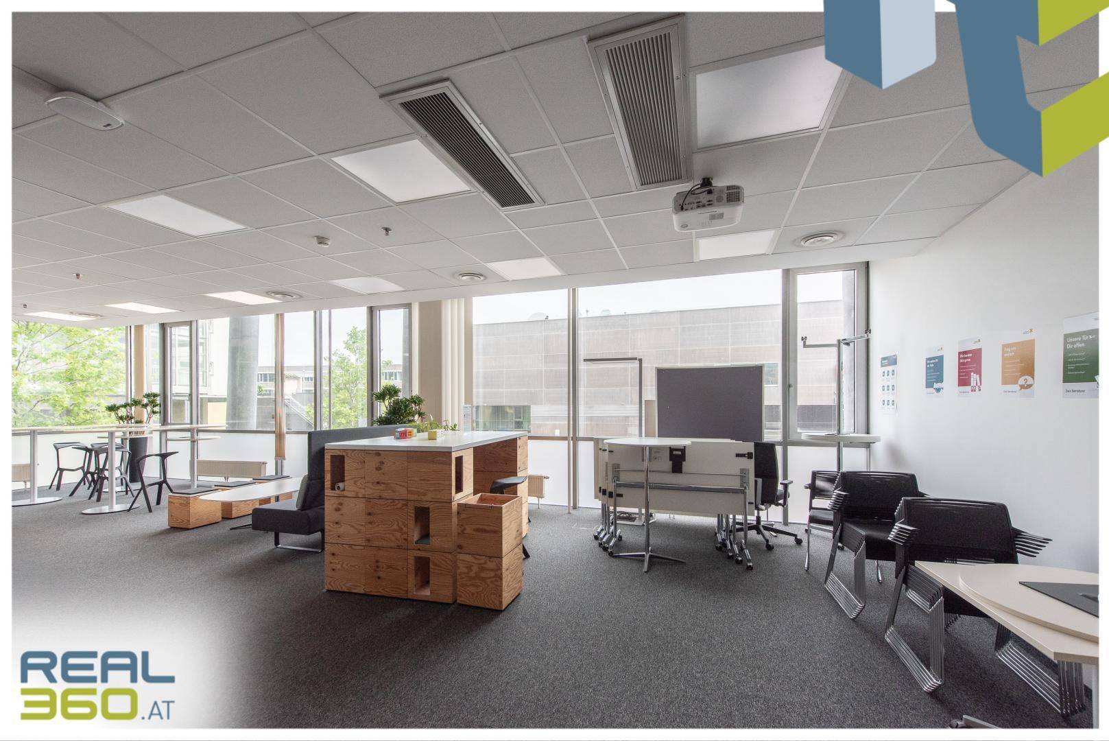 Offener Bürobereich mit Projektor, Tischen und Stühlen, umgeben von großen Fenstern.