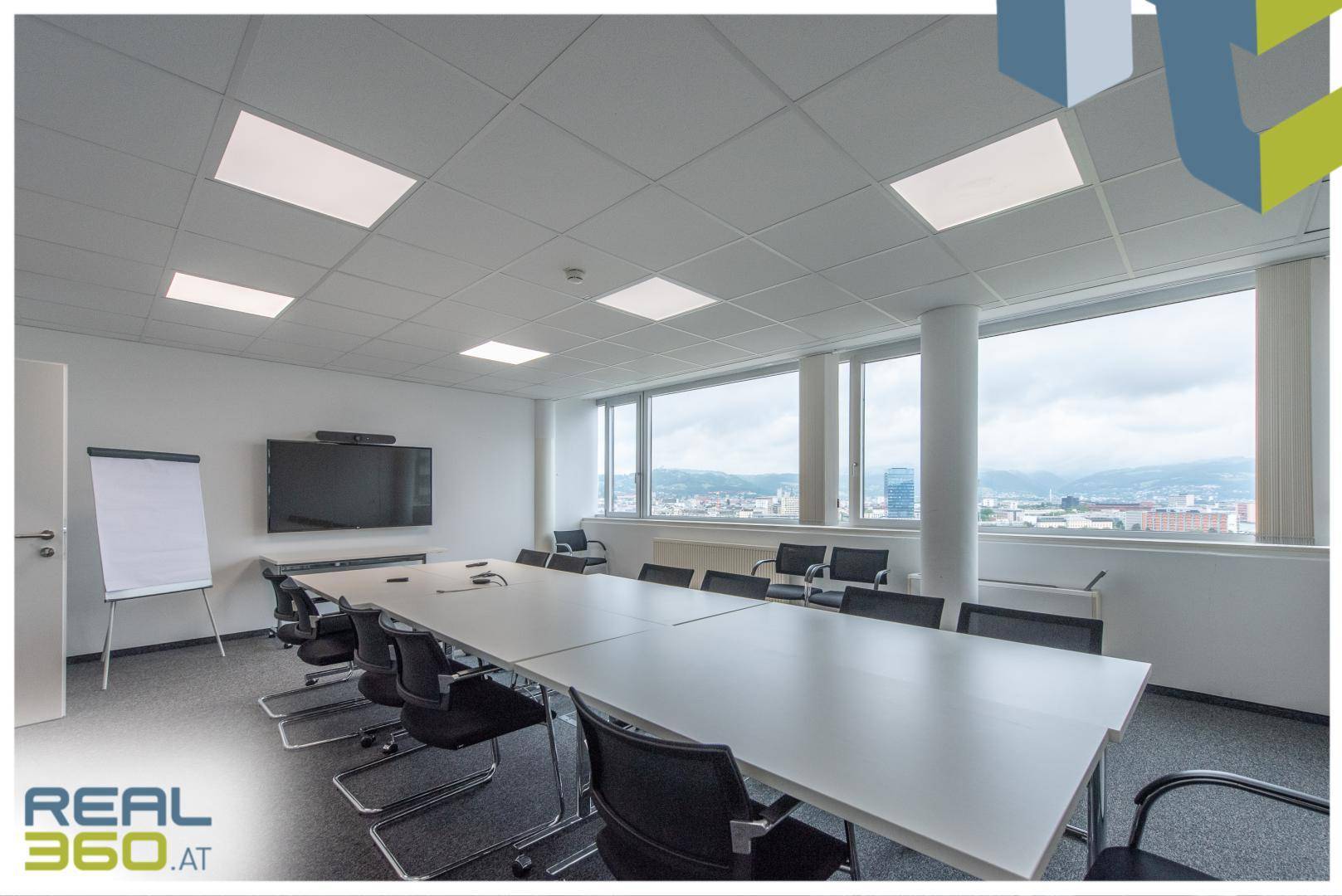 Geräumiger Konferenzraum mit großem Bildschirm, Whiteboard und weitem Stadtblick.