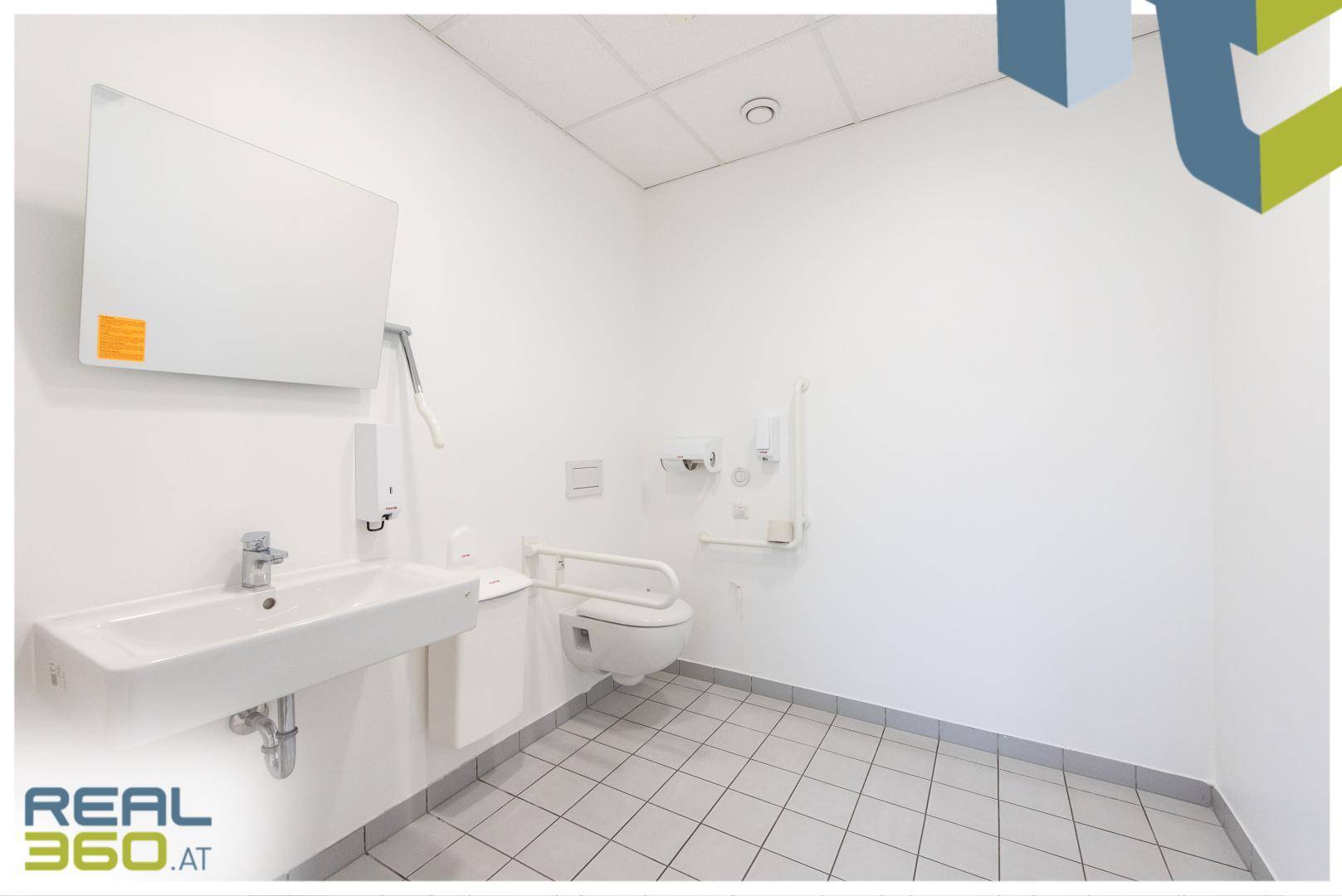 Barrierefreies Badezimmer mit Haltegriffen, wandmontierter Toilette und Waschbecken.