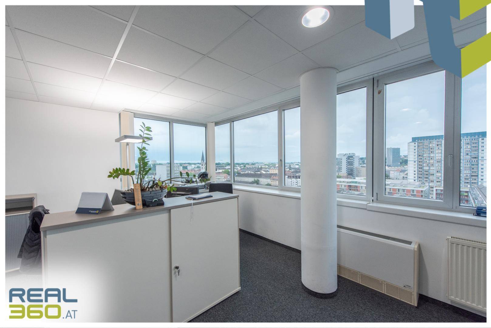 Modernes Büro mit Säule, großen Fenstern und Blick auf die städtische Umgebung.