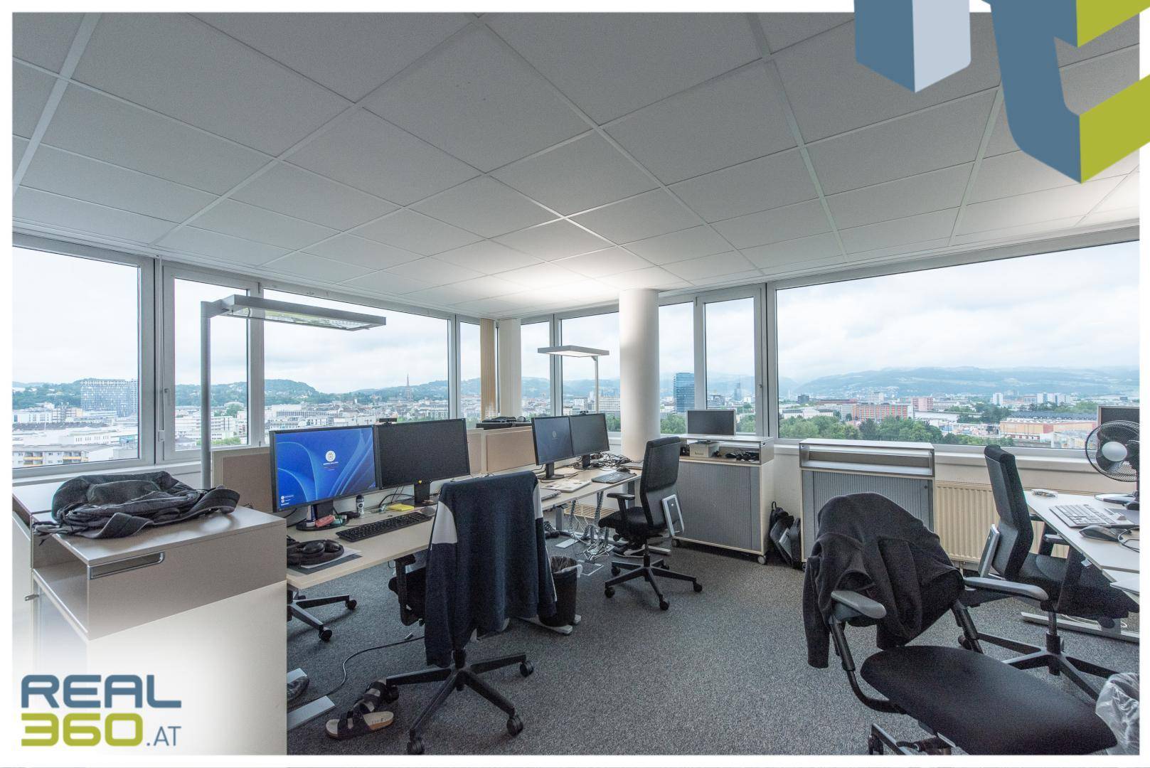 Offenes Büro mit mehreren Computern, ergonomischen Stühlen und weitem Stadtblick.