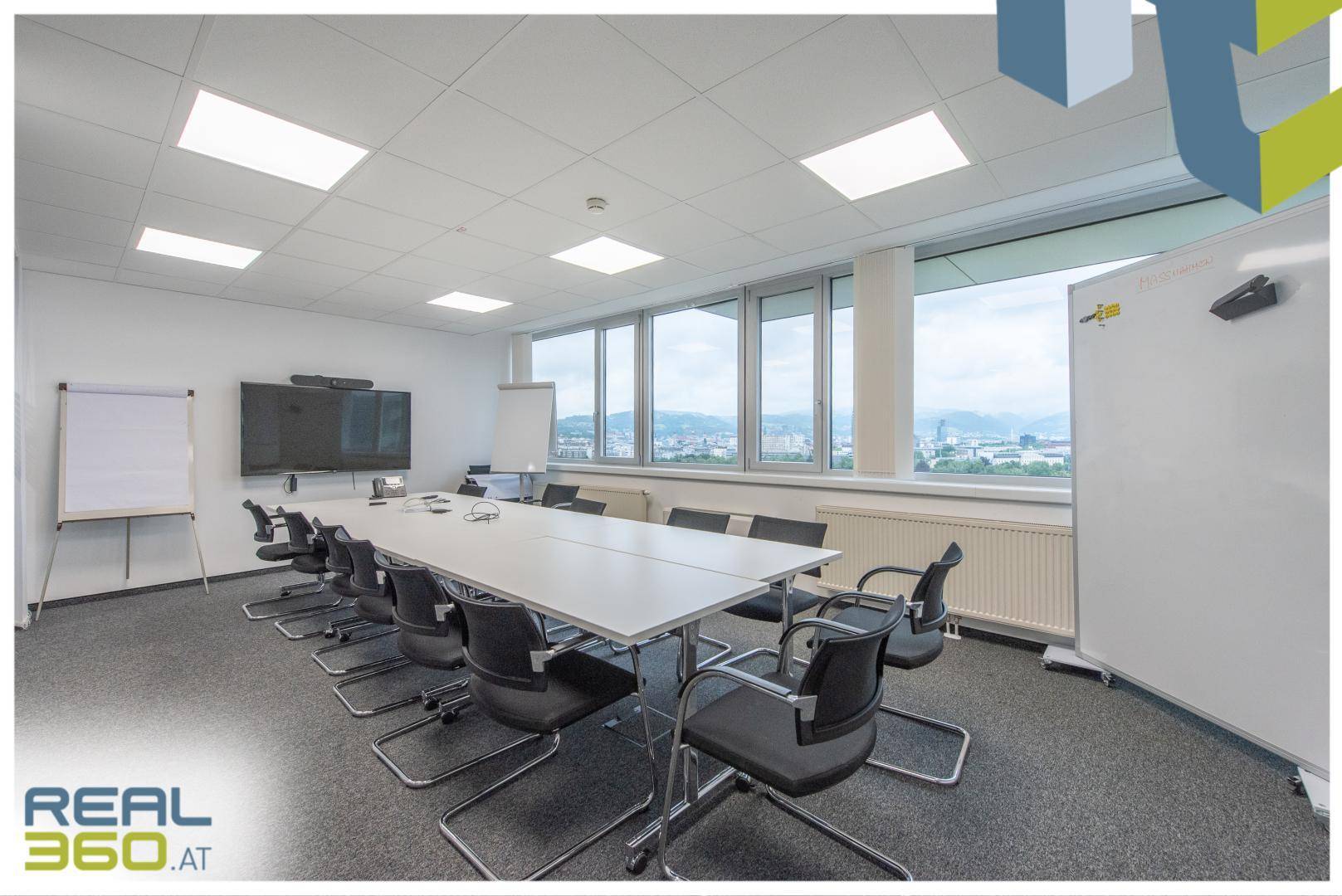 Großer Konferenzraum mit langem Tisch, vielen Stühlen und weitem Stadtblick durch die Fenster.