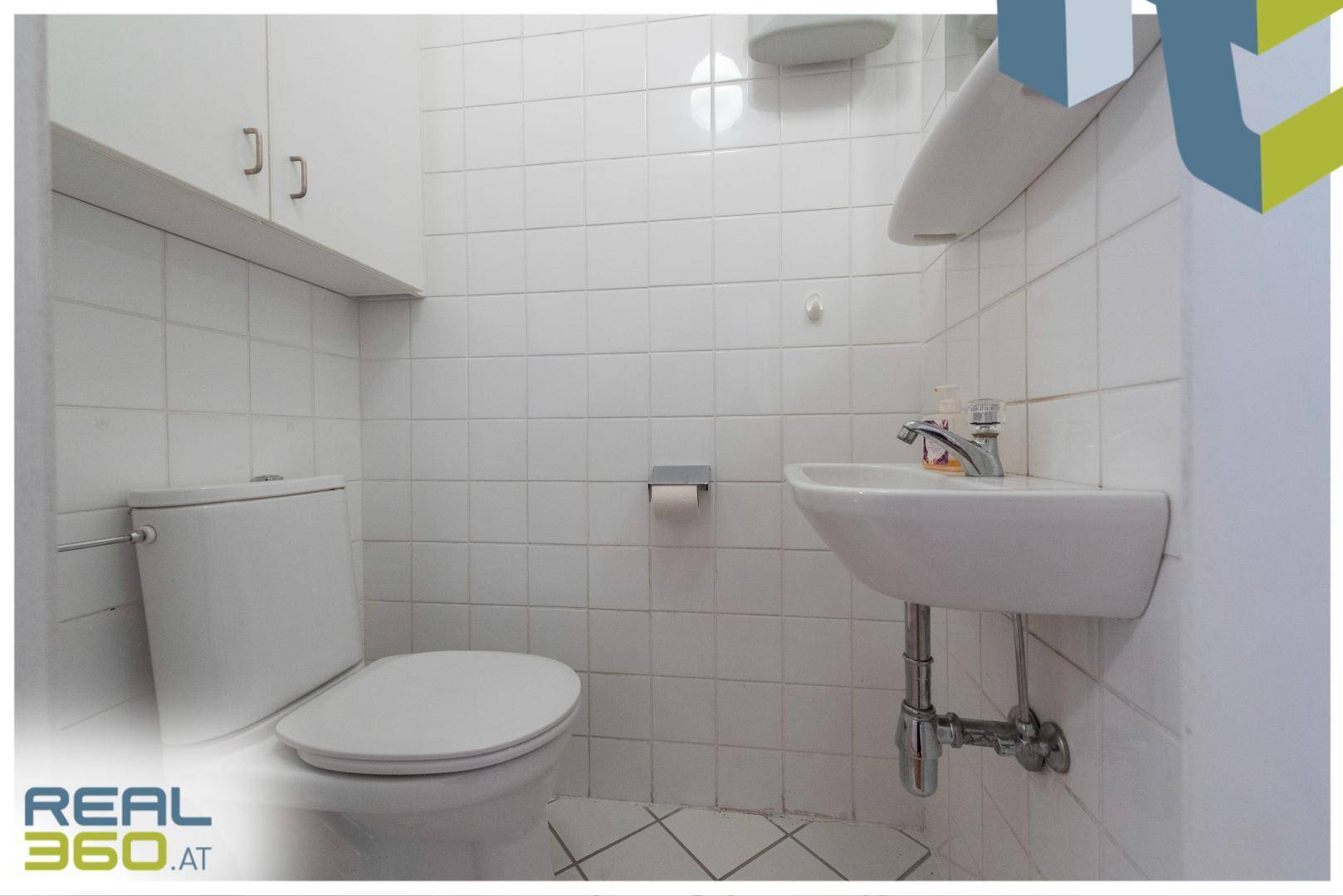 Kleines, hell gefliestes Gäste-WC mit Toilette und Handwaschbecken.