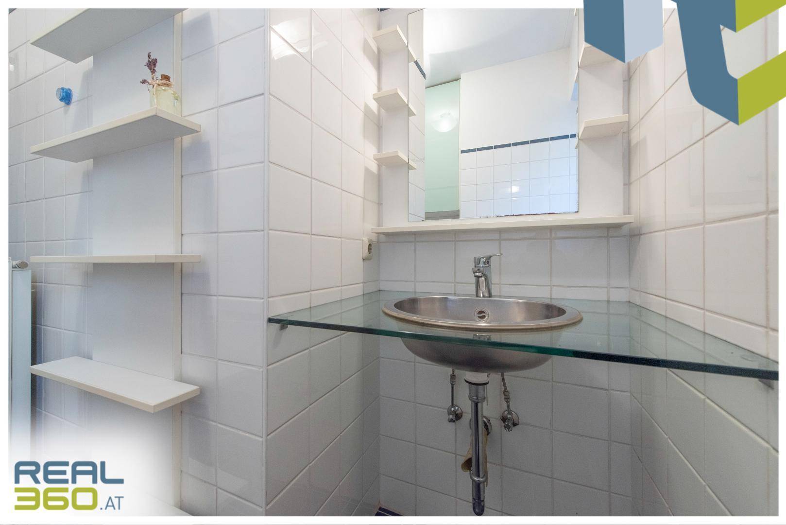 Modern gefliestes Badezimmer mit Waschbecken auf Glasplatte und Wandregalen.