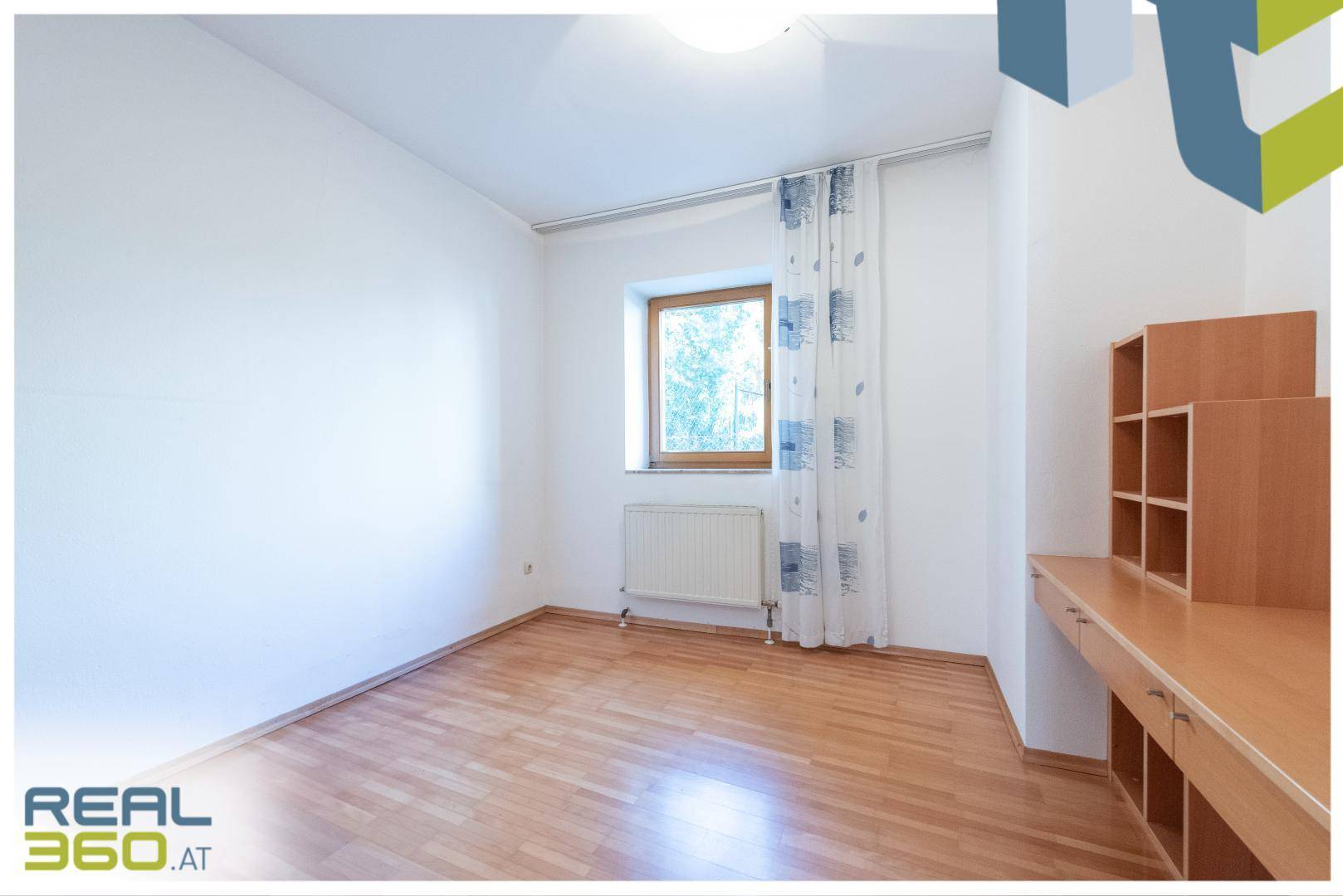 Helles Schlafzimmer mit Parkettboden, Fenster und integriertem Schreibtisch mit Regalen.