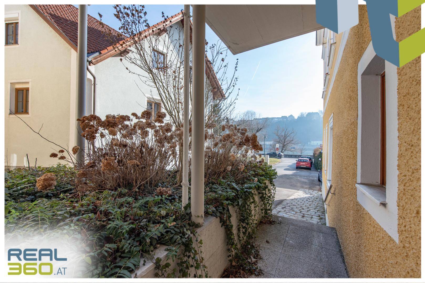 Seitlicher Zugang zum Gebäude mit Treppe, Pflanzen und Blick auf die Straße.