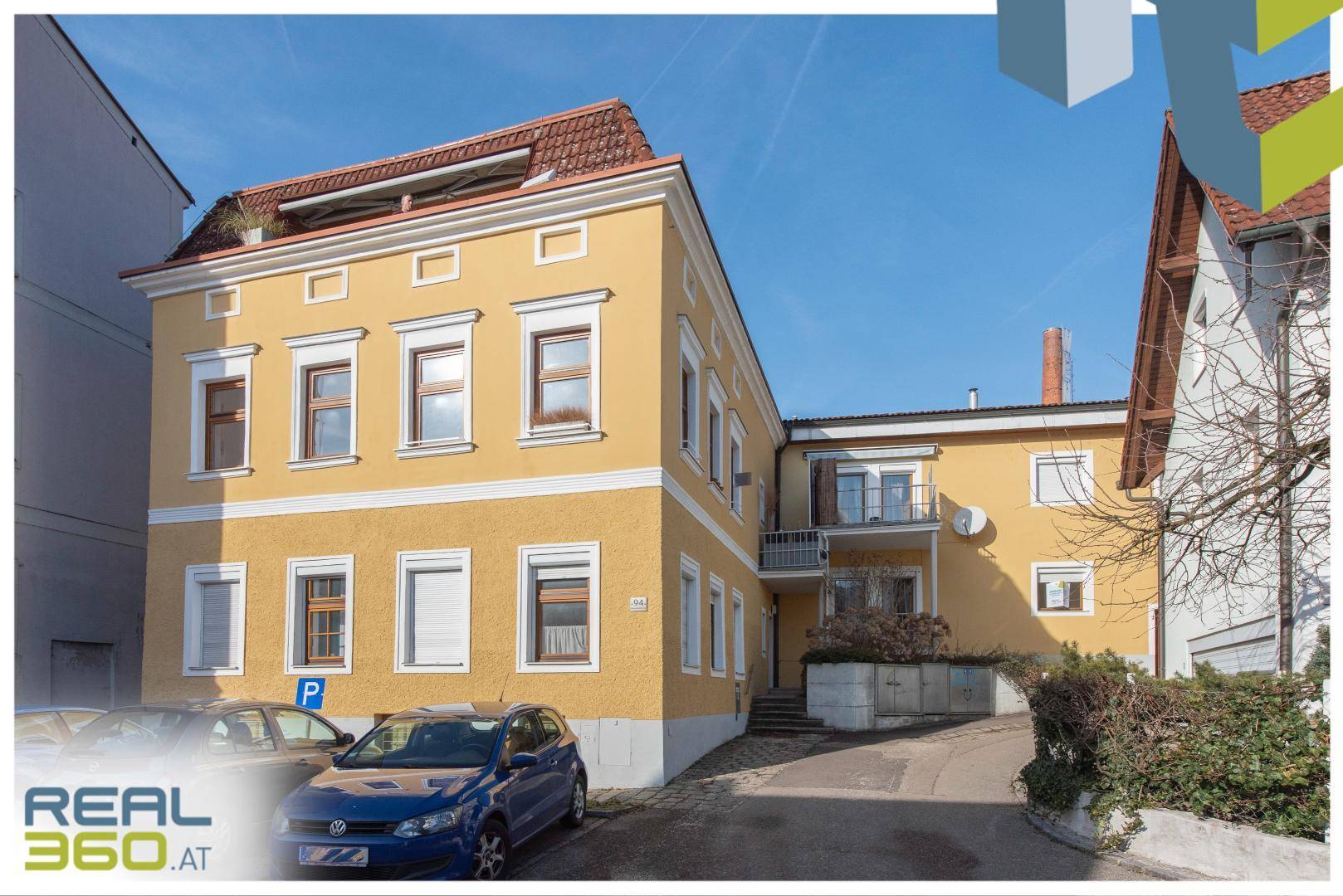 Gelbes Mehrfamilienhaus mit Parkplätzen vor dem Gebäude und klassischer Architektur.