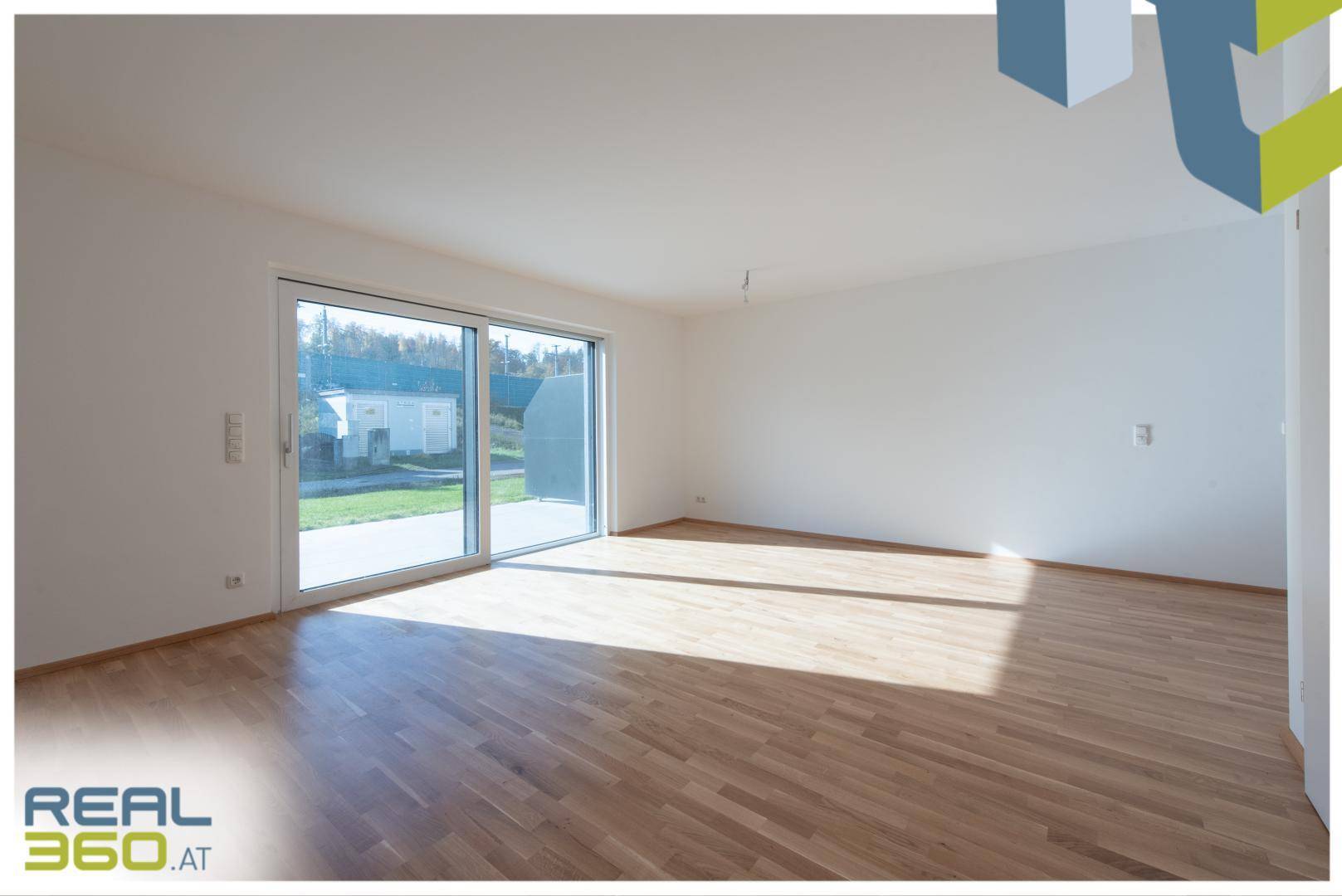 Lichtdurchfluteter Raum mit Holzboden und Zugang zu einem Außenbereich.