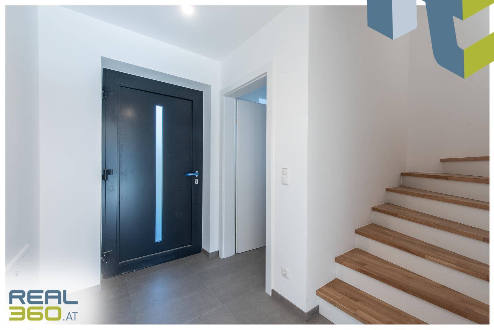 Eingangsbereich mit Fliesenboden, moderner Haustür und Holztreppe zum Obergeschoss.