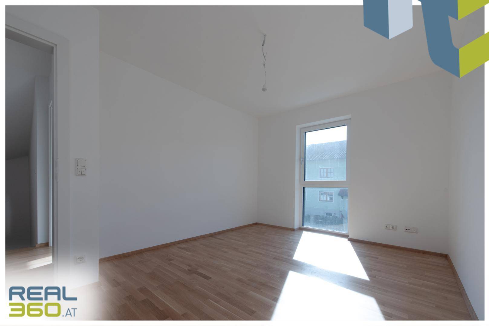Helles Zimmer mit Holzboden und Fenster, das einen Blick nach draußen bietet.