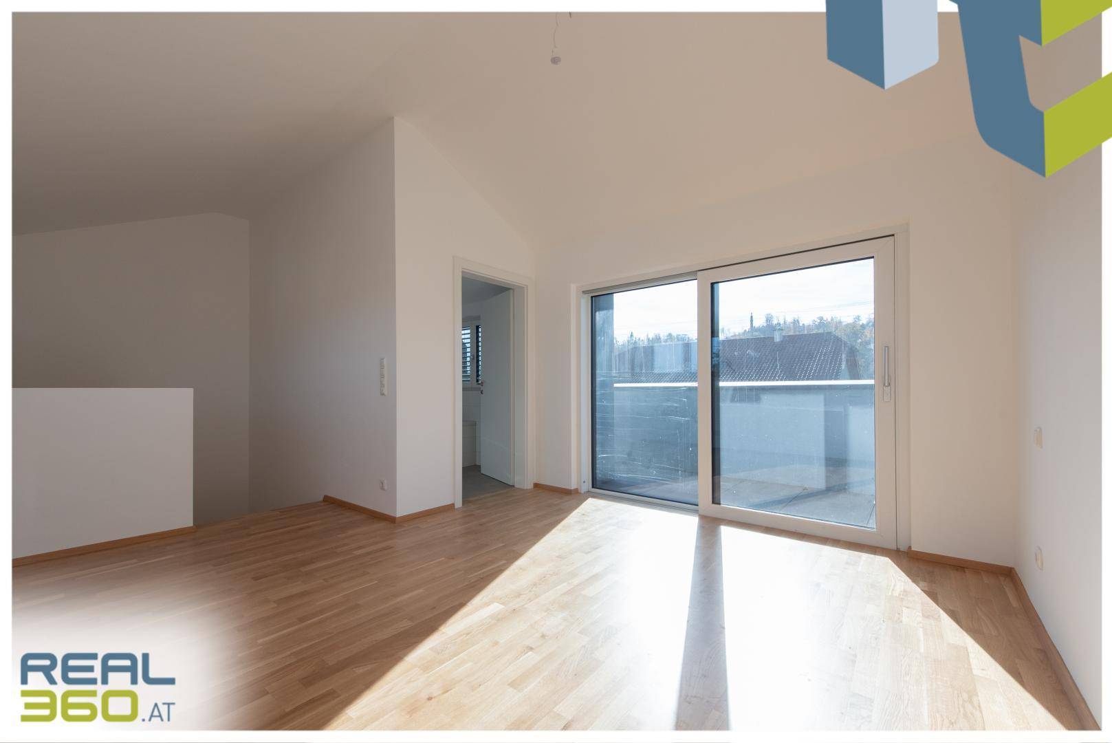 Geräumiges Zimmer im Obergeschoss mit Holzboden und Schiebetür zum Balkon.
