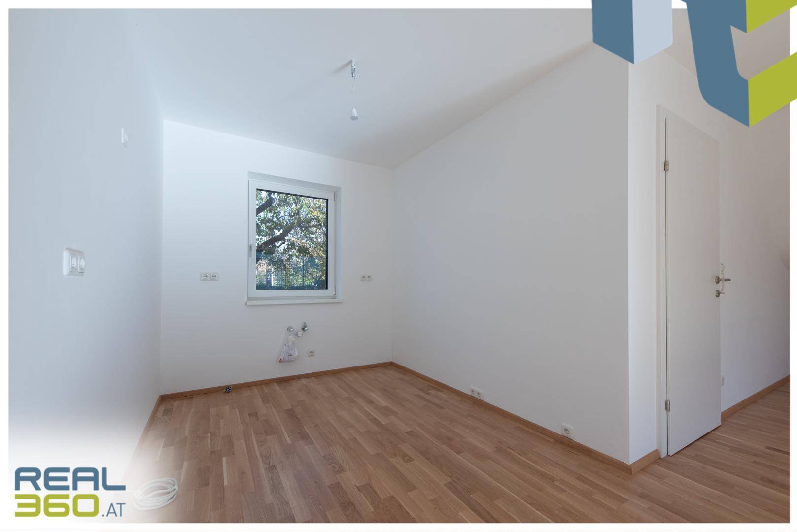 Helles Zimmer mit Holzboden und einem Fenster, das viel Tageslicht hereinlässt.