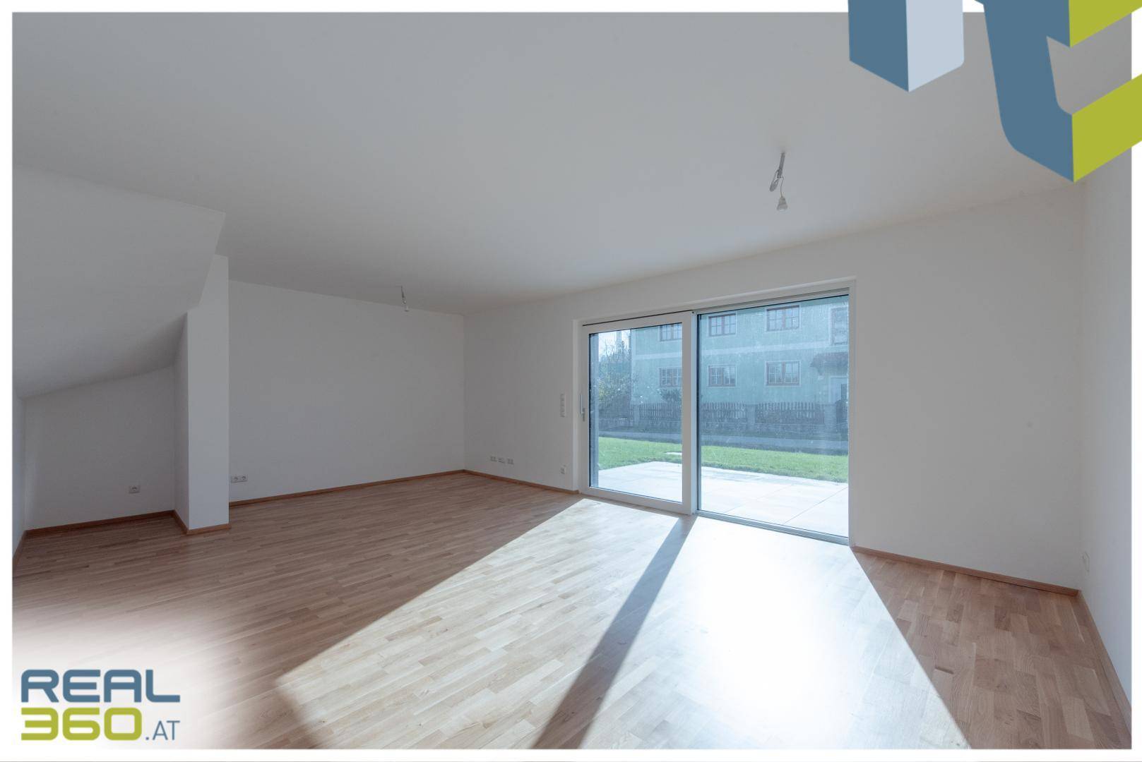 Geräumiges Wohnzimmer mit Holzboden und großer Schiebetür zum Gartenbereich.