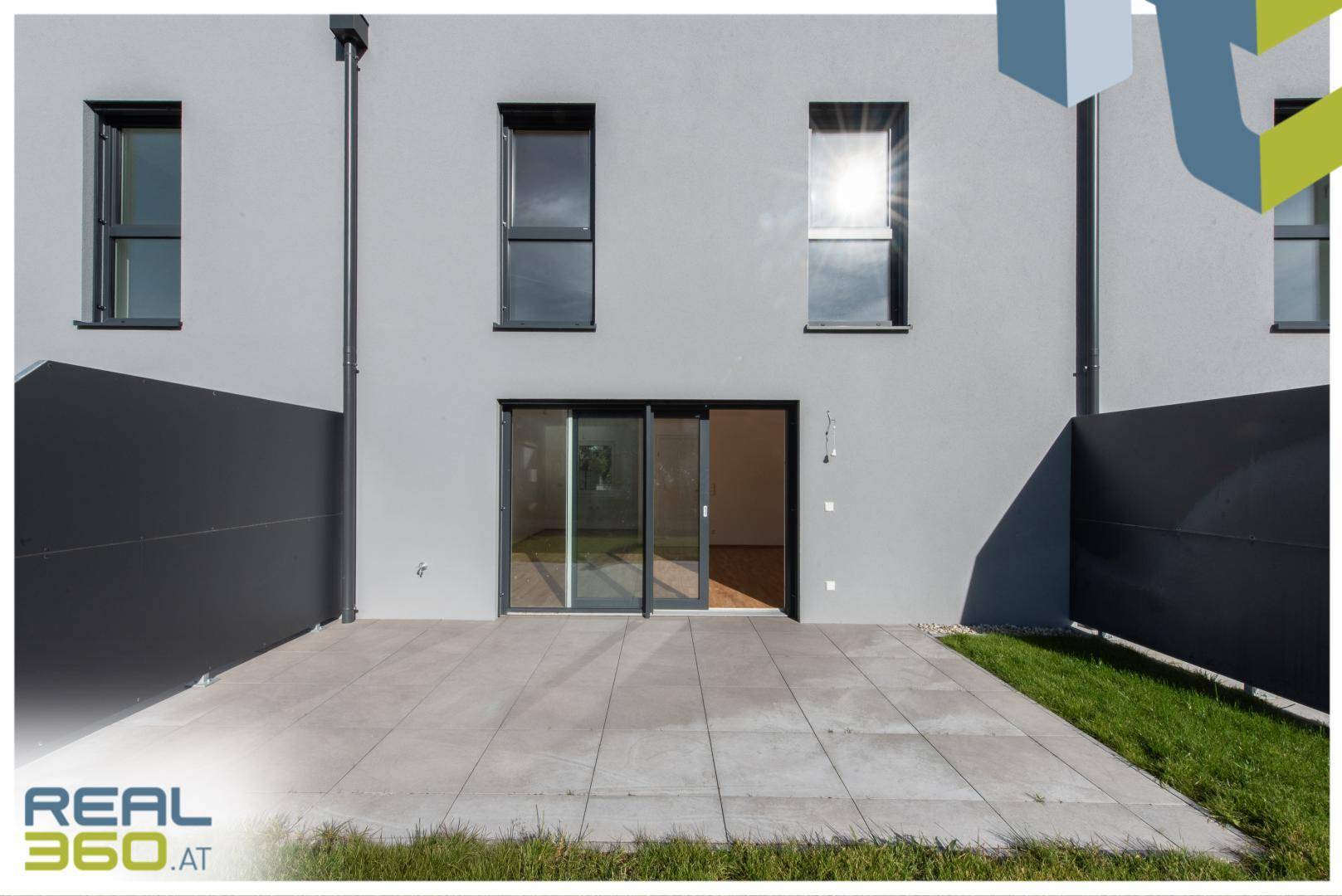 Rückseite des Hauses mit großer Schiebetür und gepflasterter Terrasse.