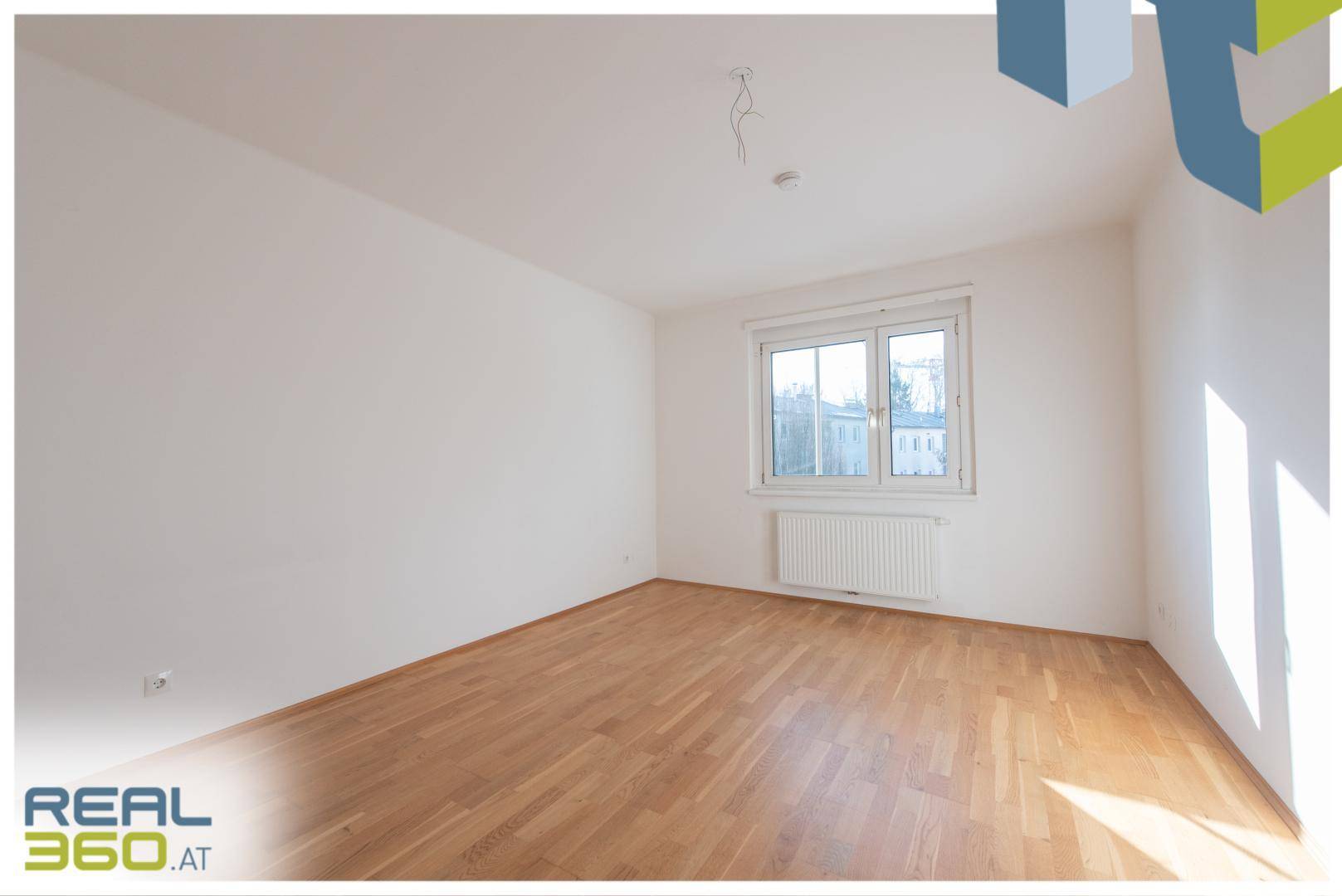 Sonniger Raum mit Parkettboden und großem Fenster, das viel Tageslicht bietet.