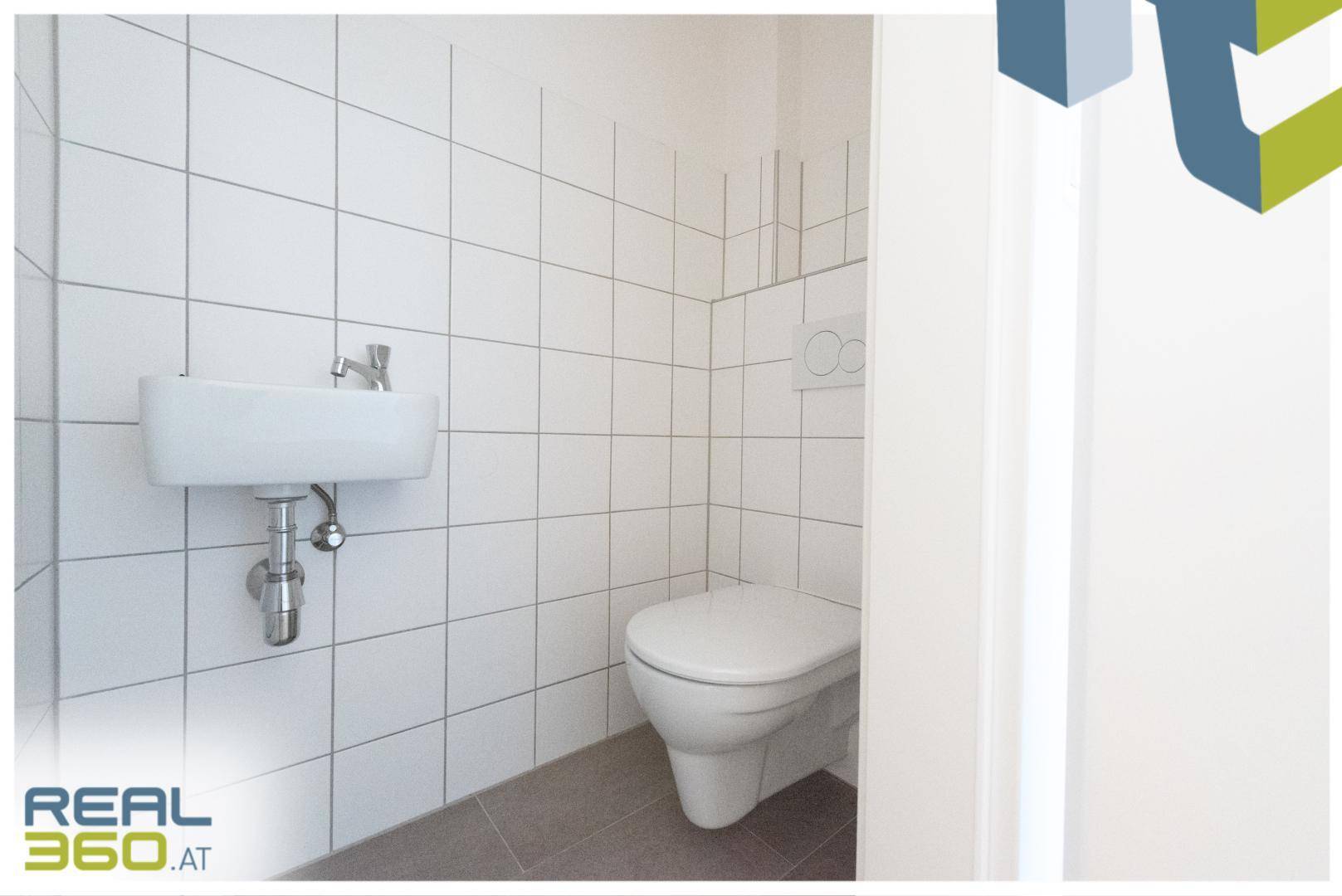 Separates WC mit wandhängender Toilette und kleinem Waschbecken, komplett gefliest.