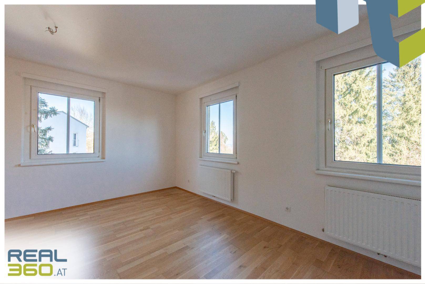 Helles Schlafzimmer mit Parkettboden und mehreren Fenstern, die viel Tageslicht hereinlassen.