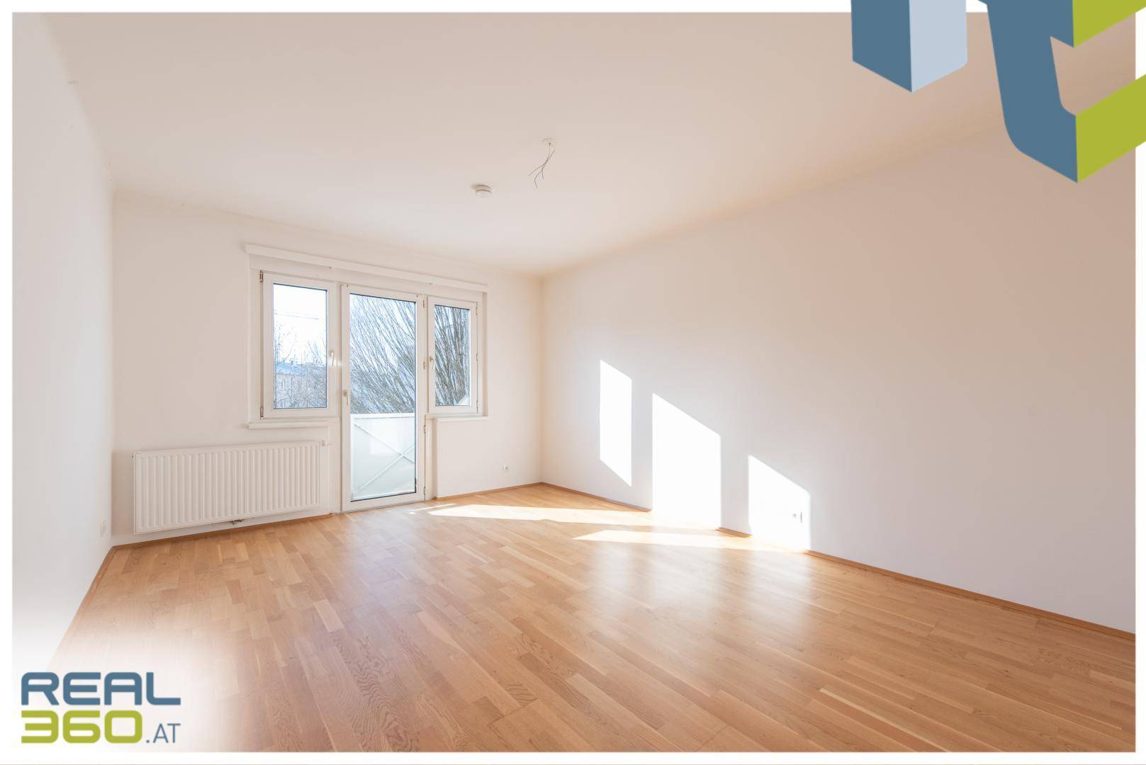 Lichtdurchflutetes Wohnzimmer mit Parkettboden und Zugang zu einem sonnigen Außenbereich.