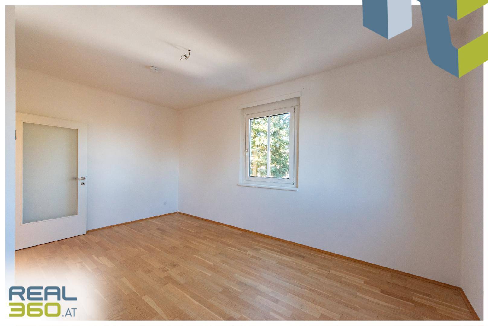 Ruhiges Zimmer mit Parkettboden, einem Fenster und einer modernen Tür mit Glaseinsatz.