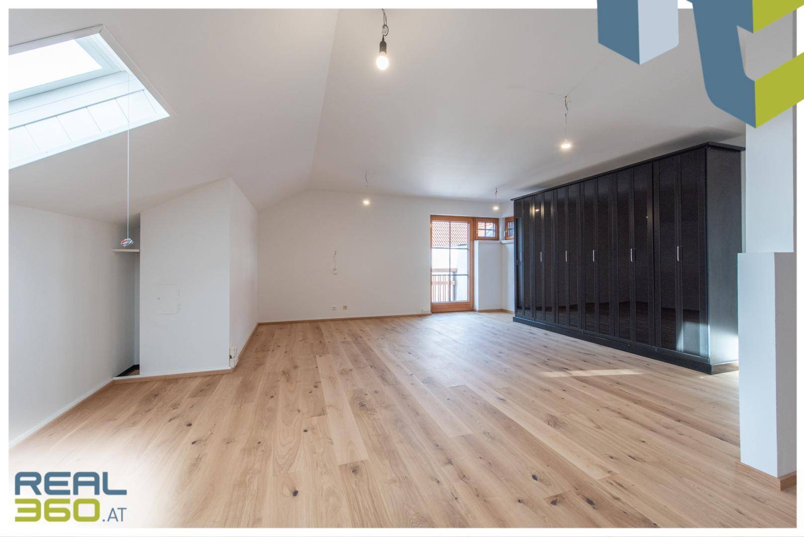 Helles Zimmer mit Holzboden, Dachfenster und integriertem Kleiderschrank im Dachgeschoss.