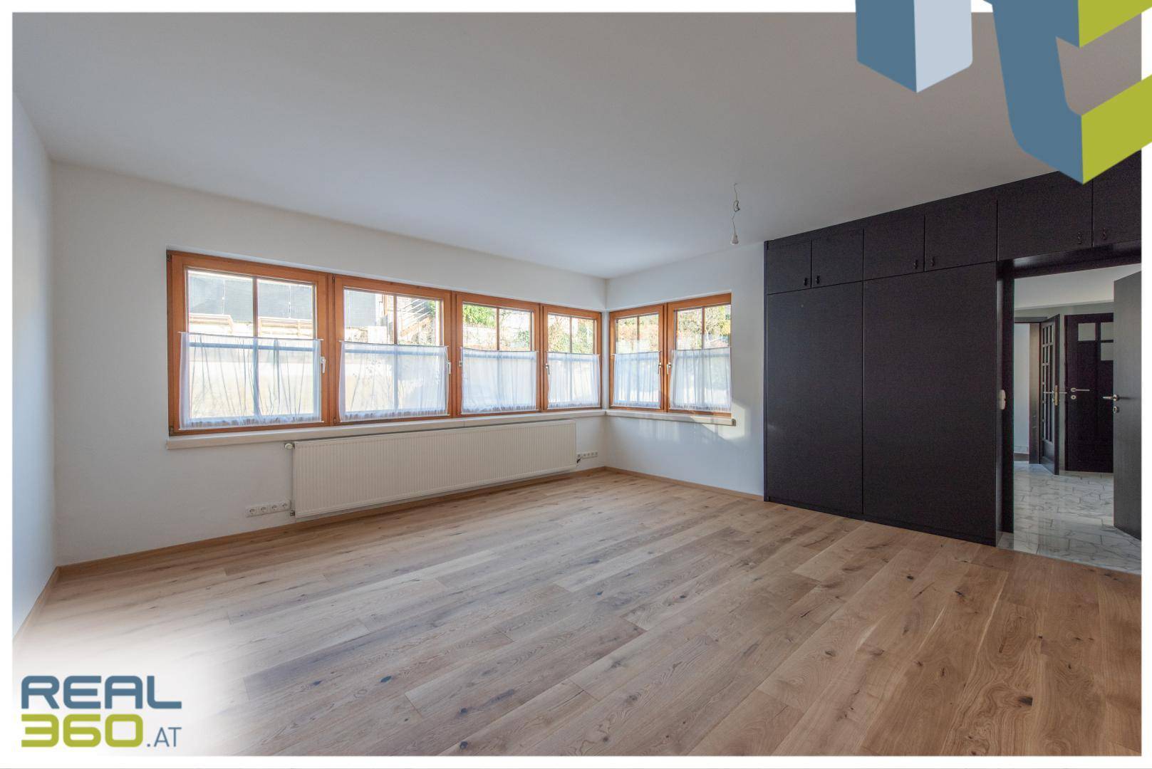 Geräumiges Zimmer mit hellem Holzboden und vielen Fenstern, bereit zur individuellen Gestaltung.