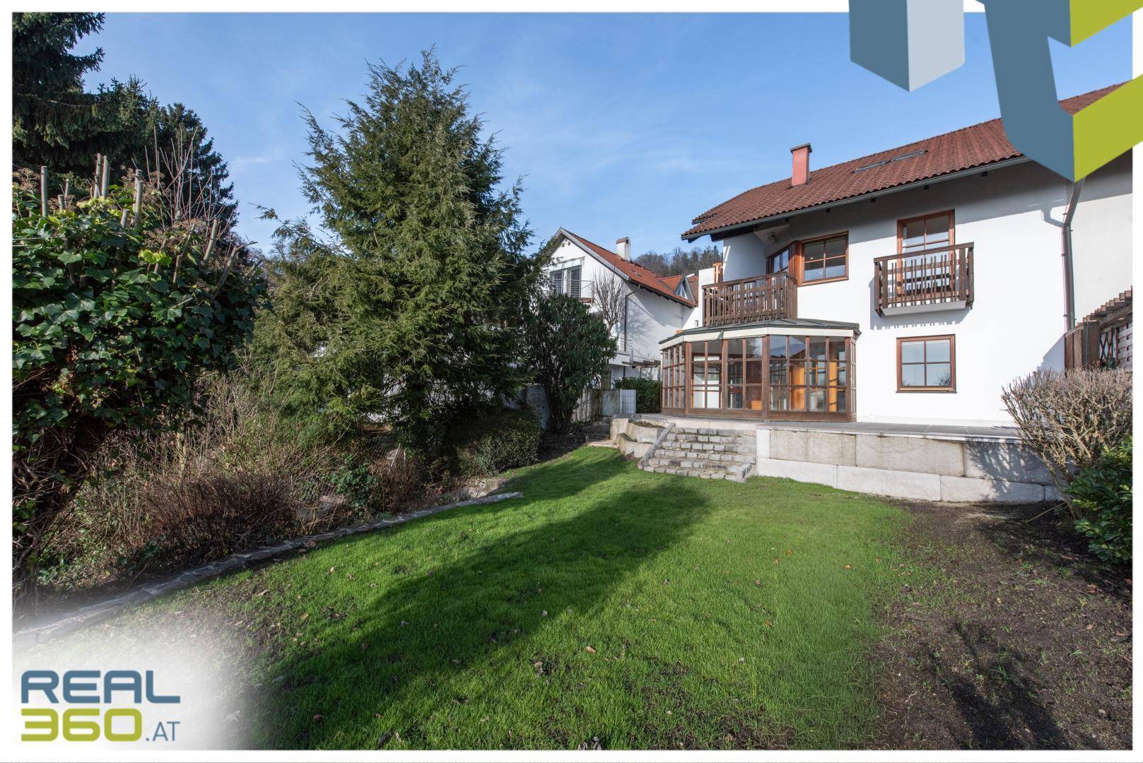Hausansicht von der Gartenseite mit Wintergarten und weitläufiger Rasenfläche.