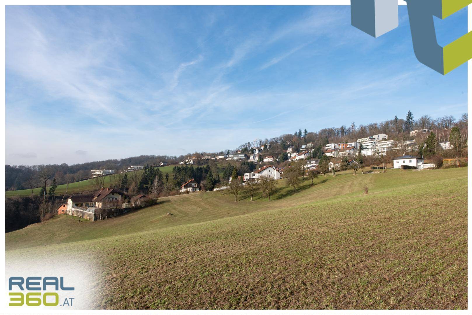 Weitläufige grüne Landschaft mit vereinzelten Häusern unter blauem Himmel.