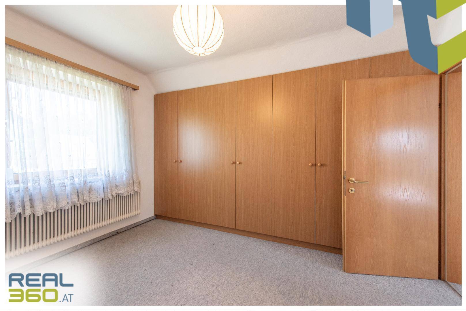 Schlafzimmer mit großem Einbauschrank, Teppichboden und viel Tageslicht.