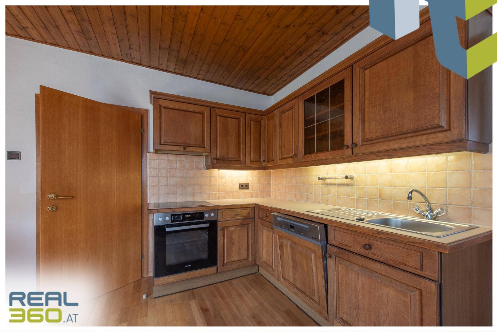 Detailansicht der Holzküche mit Backofen, Spülmaschine und gefliestem Spritzschutz.