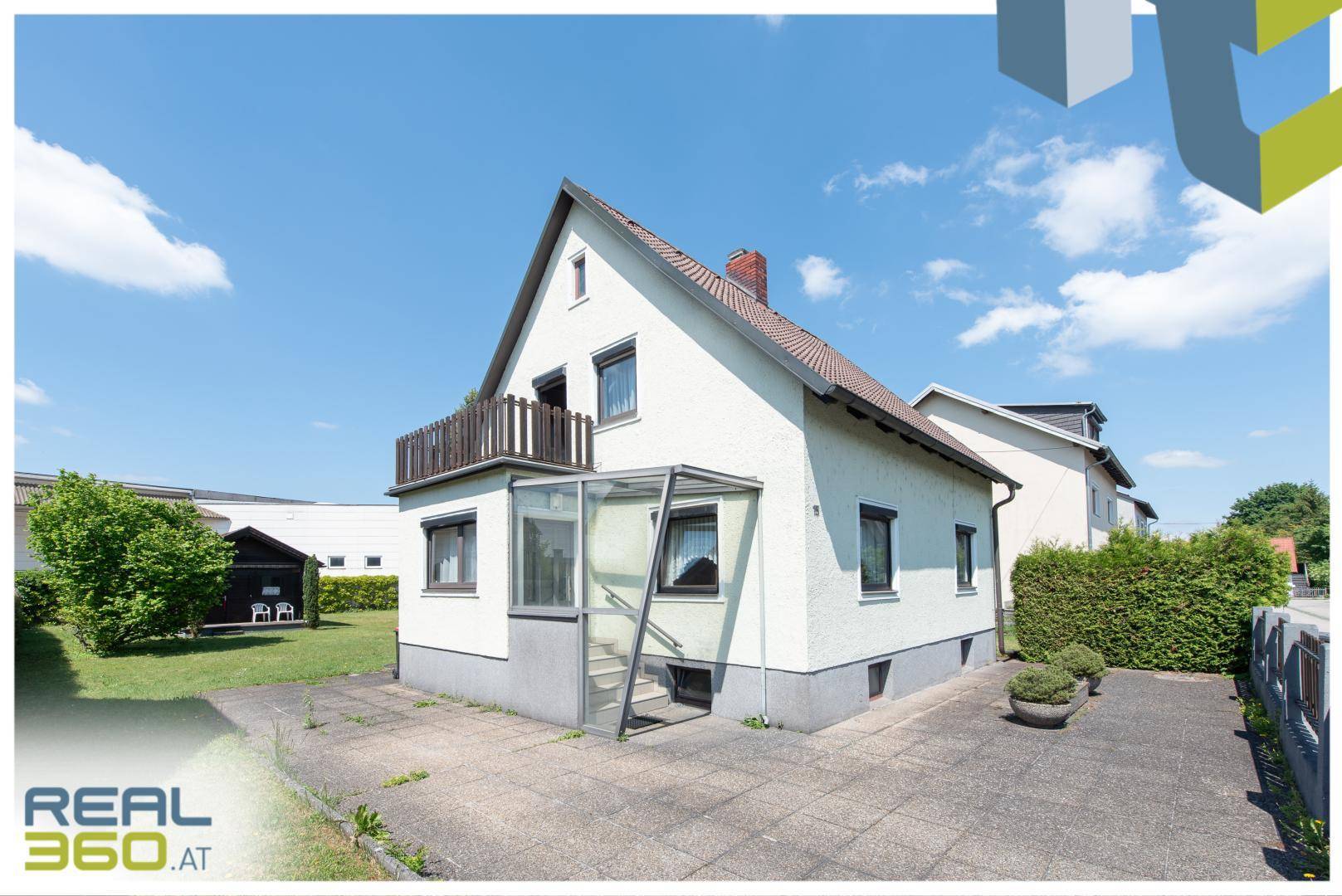 Seitenansicht des Hauses mit gepflasterter Einfahrt, Kellerzugang und Balkon im Obergeschoss.