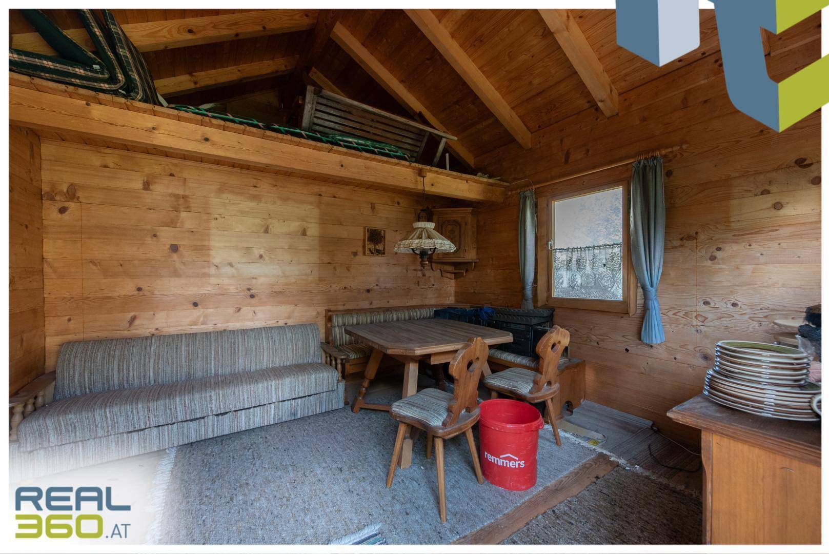 Rustikaler Wohnbereich in einer Holzhütte mit Holzwänden, Holzbalken und gemütlicher Sitzecke.