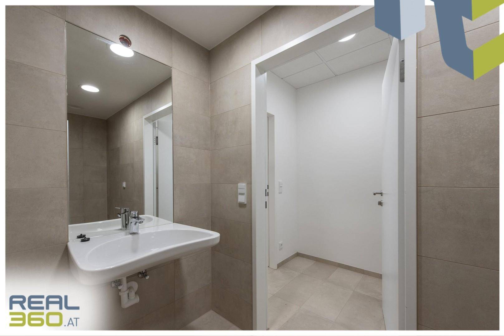 Modernes Badezimmer mit Waschbecken, Spiegel und Zugang zu einem weiteren Raum.