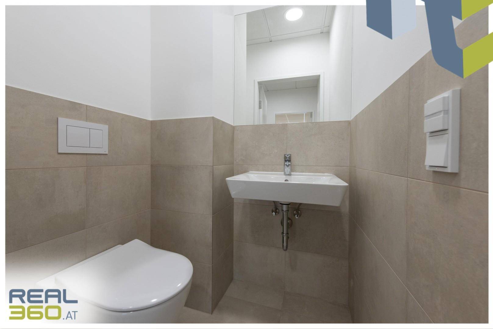 Gäste-WC mit modernem Hänge-WC, kleinem Waschbecken und beigefarbenen Fliesen.