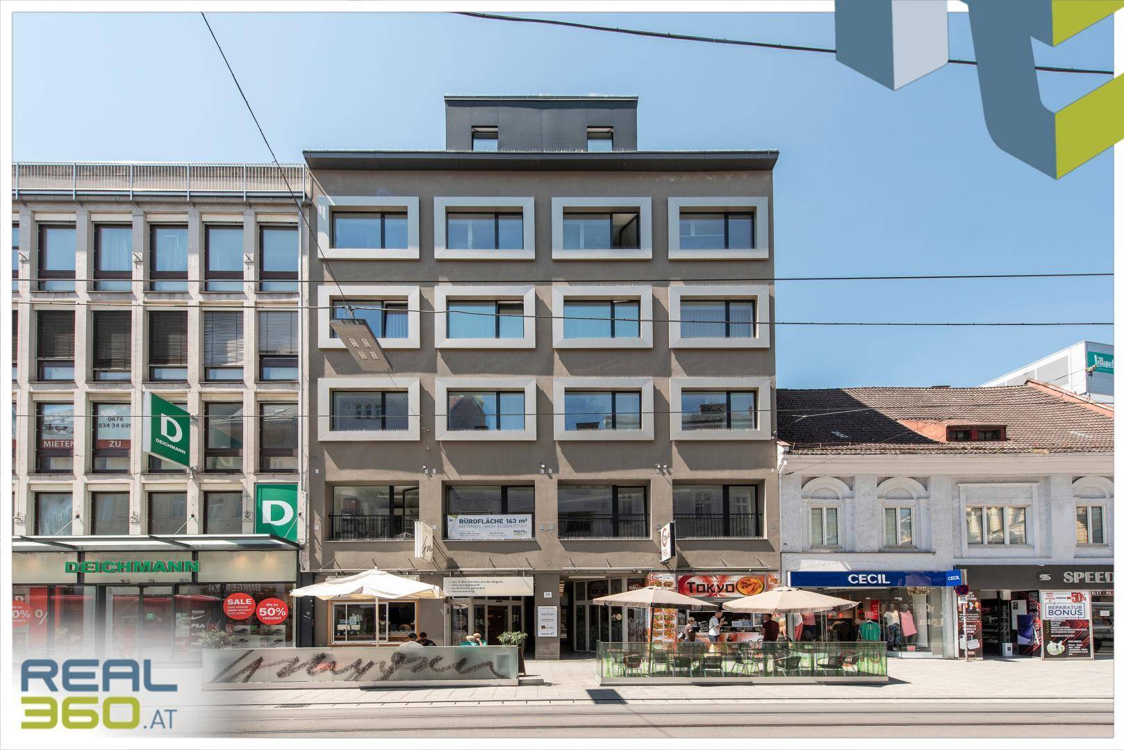 Moderne Geschäftsfassade mit großen Fenstern und Außengastronomie in belebter Stadtlage.