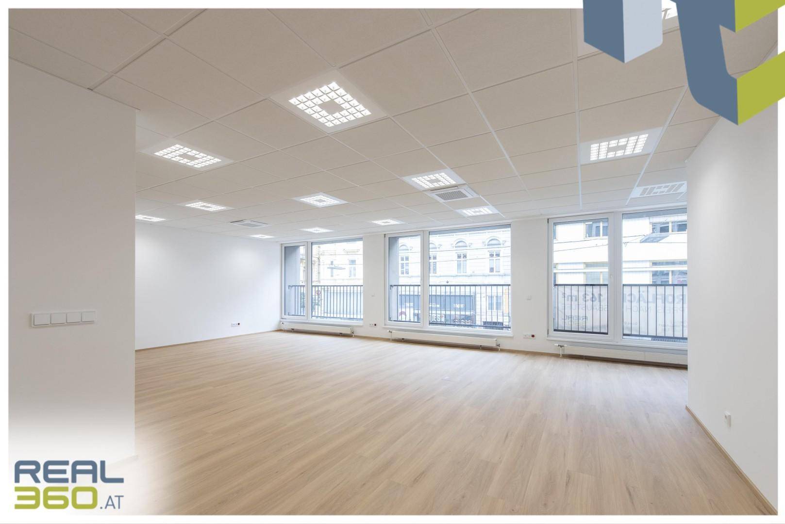 Heller Büroraum mit großen Fenstern, die viel Tageslicht hereinlassen, und modernem Laminatboden.
