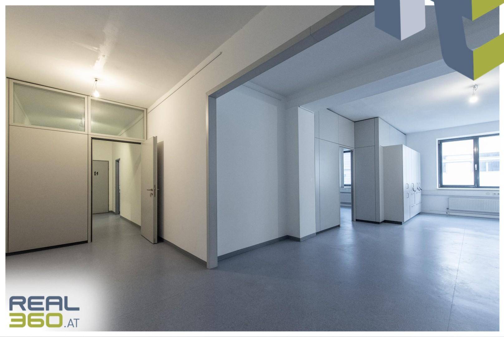 Heller, offener Bürobereich mit Zugang zu einem Flur, ausgestattet mit modularen Wänden und grauem Boden.
