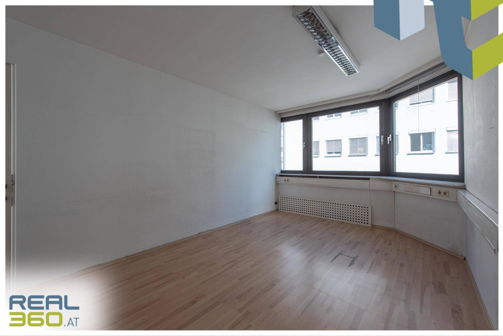 Geräumiges Büro mit Holzboden, großen Fenstern und Blick auf die Stadt.